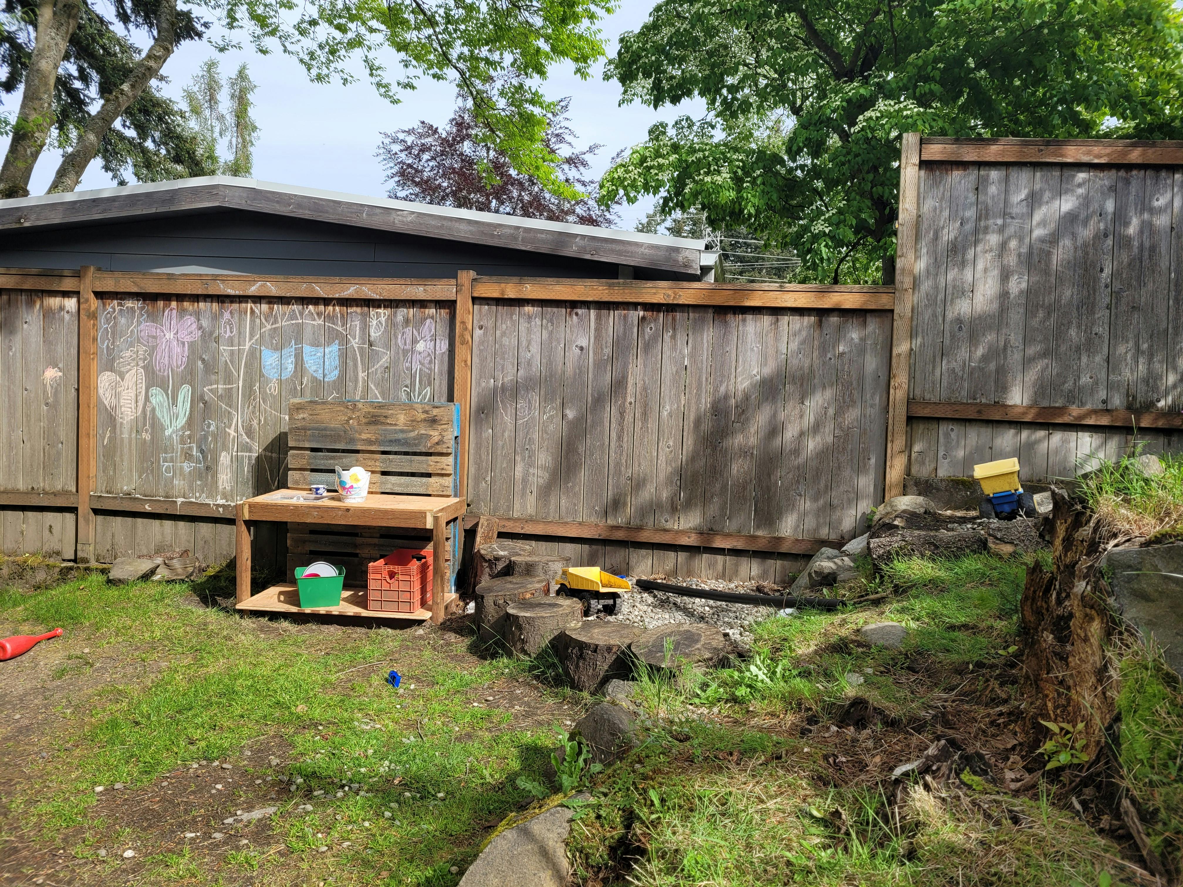 Outdoor play area with a wooden fence, play kitchen, and toy trucks