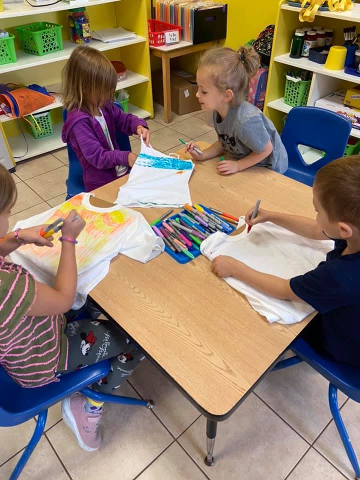 Children decorating t-shirts with markers at a table