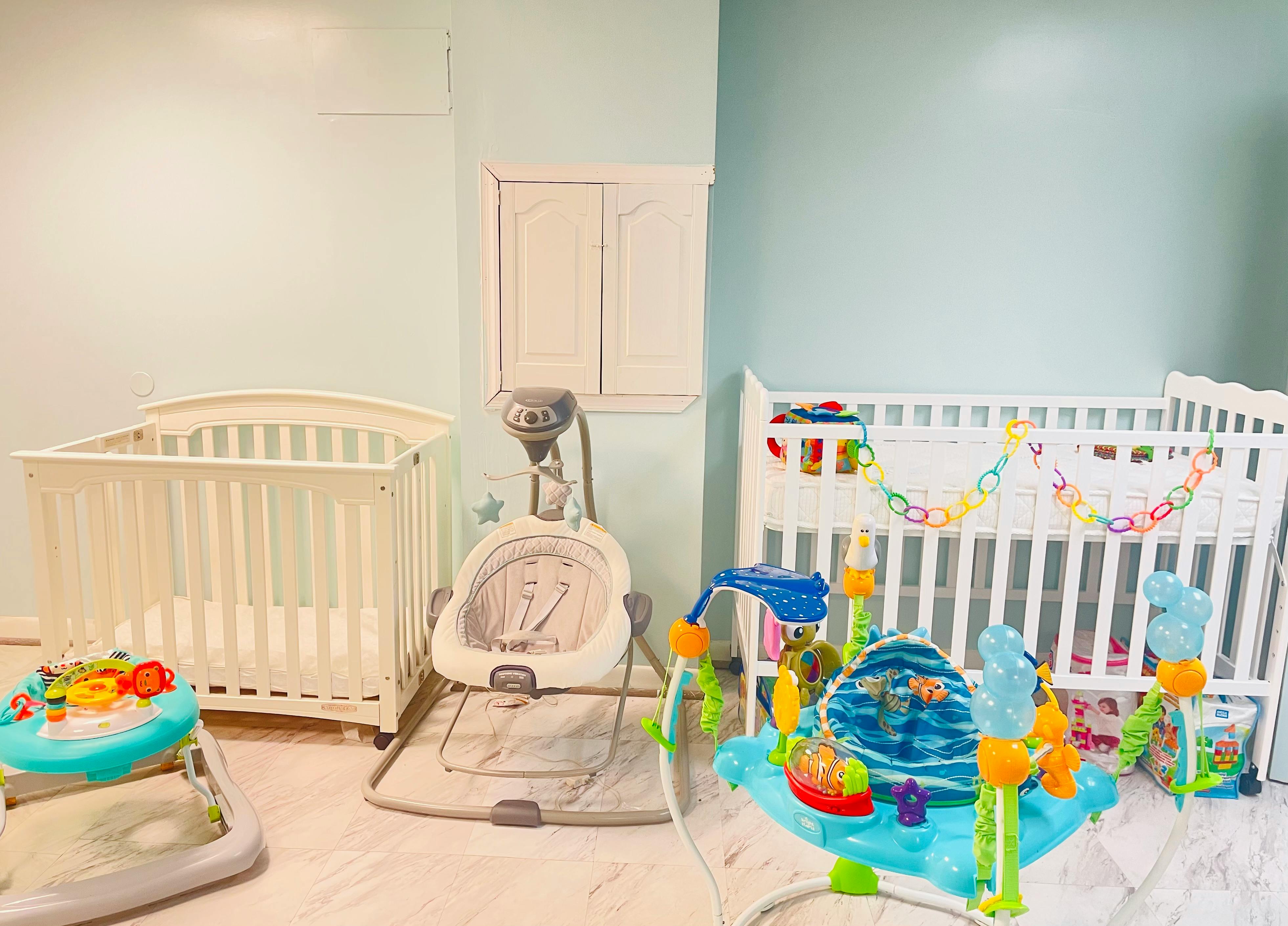 Two cribs and baby play equipment in a room