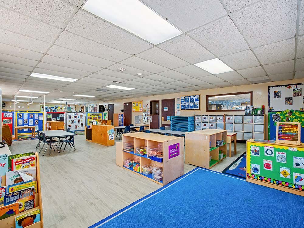 An empty early childhood classroom with tables, chairs, and learning materials
