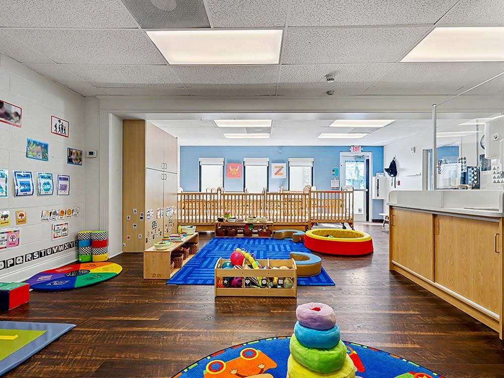 Classroom with cribs, play rugs, and storage cabinets