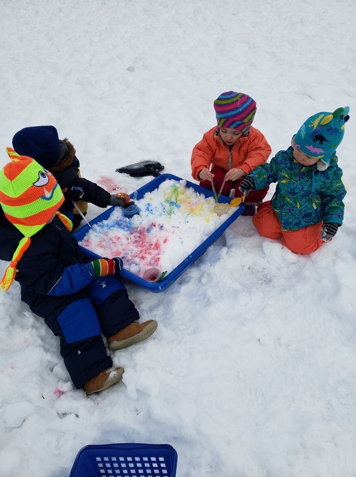 Three children playing with colored snow in a blue tray