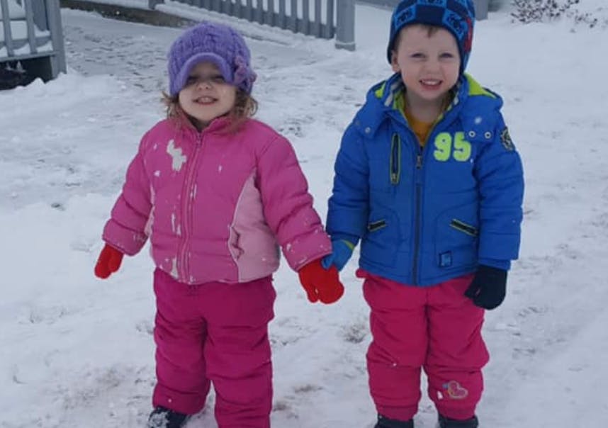 Two children in winter clothing holding hands in the snow