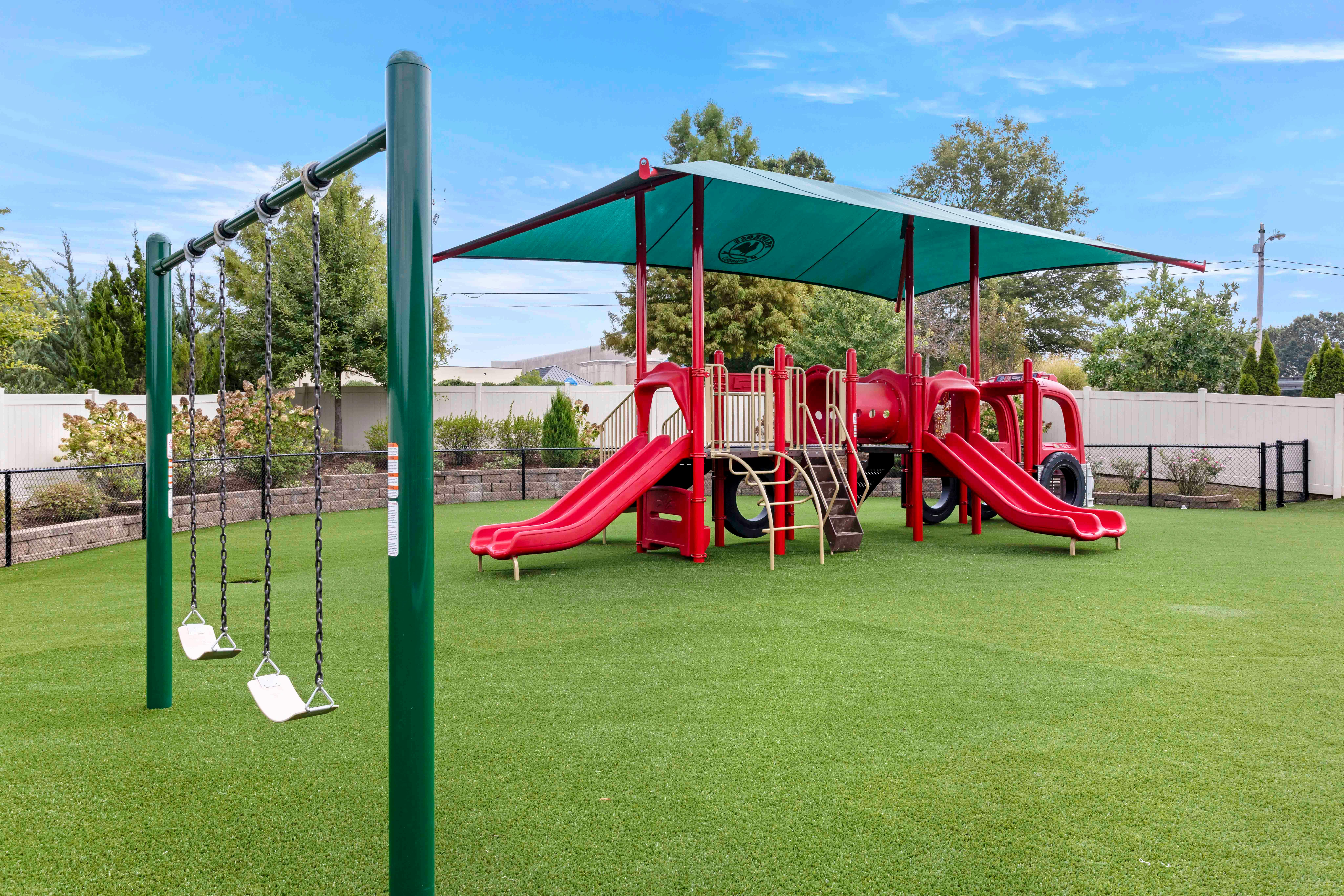 red playground structure with slides and a swing set on artificial grass