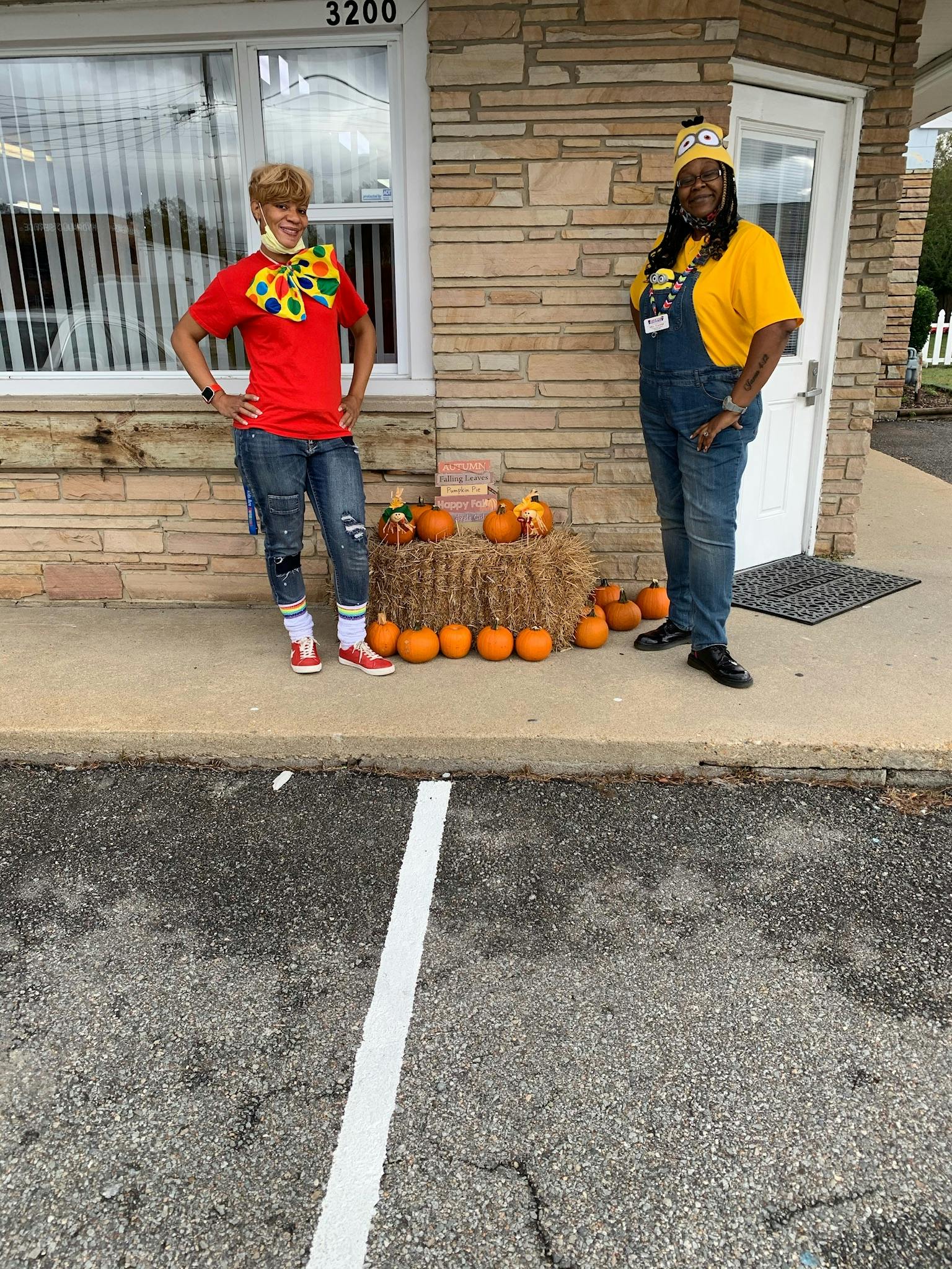 Two people standing outside next to a hay bale and pumpkins