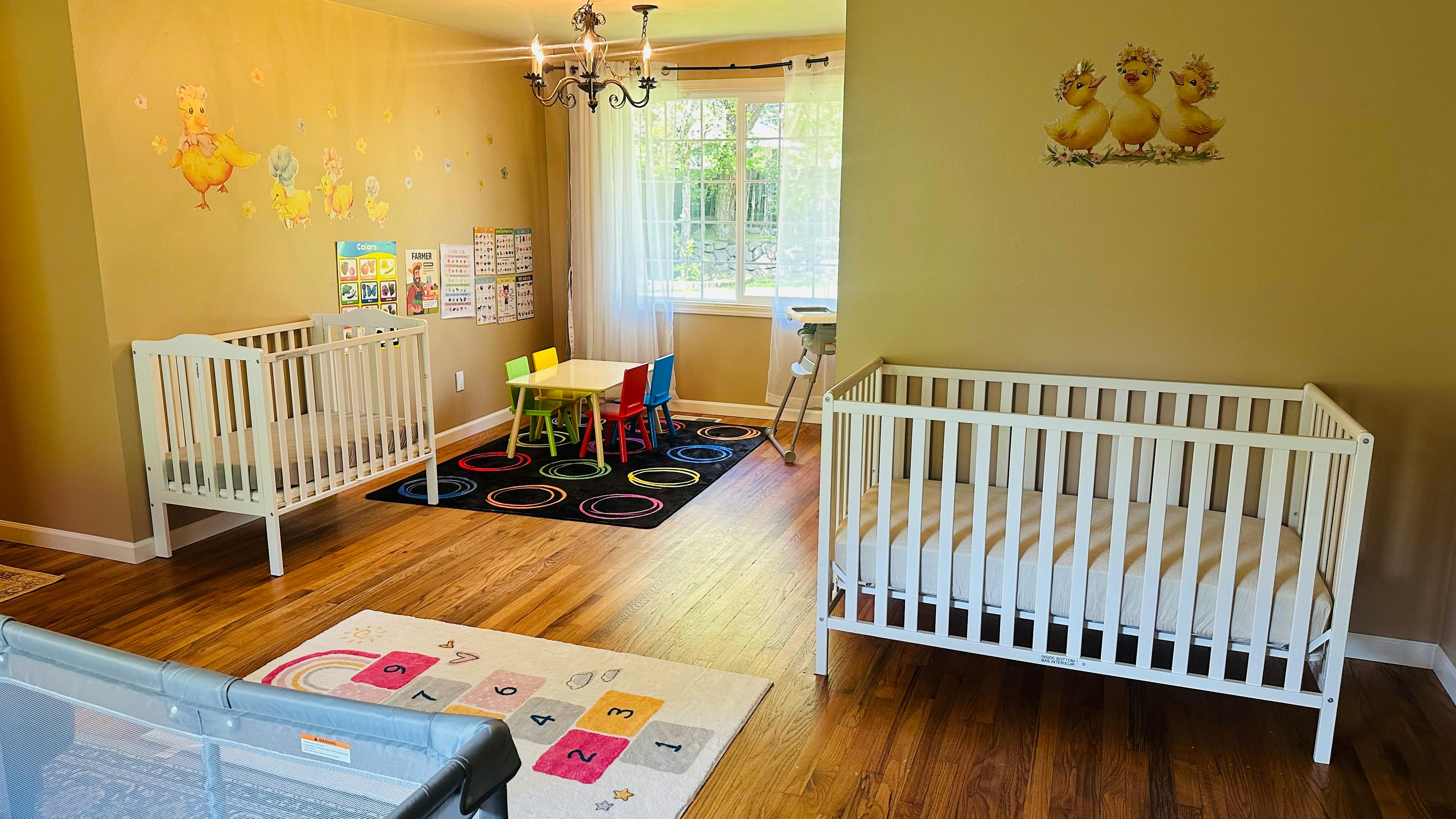 Two white cribs in a room with a small table and chairs