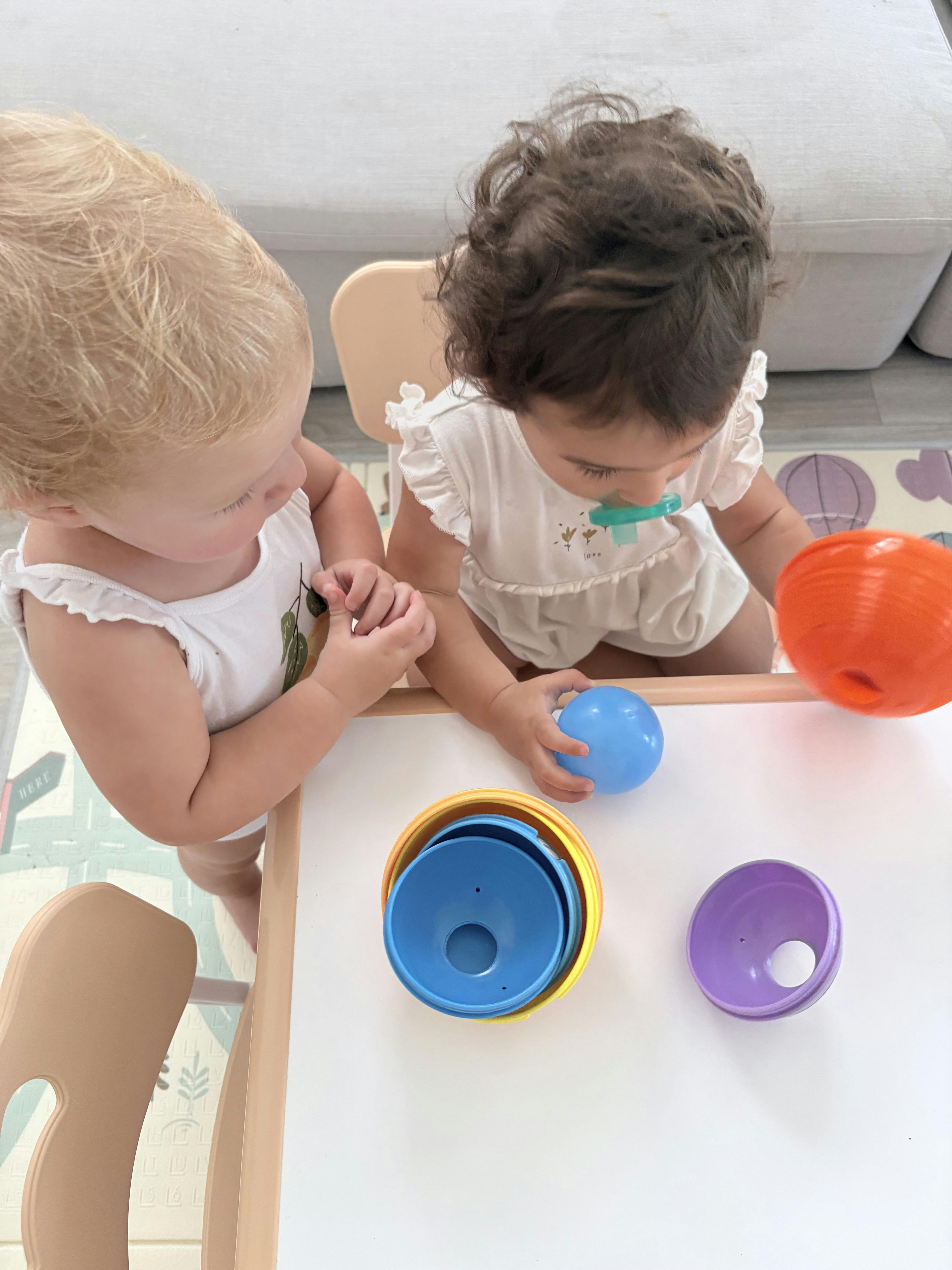 Two young children playing with colorful stackable bowls at a table