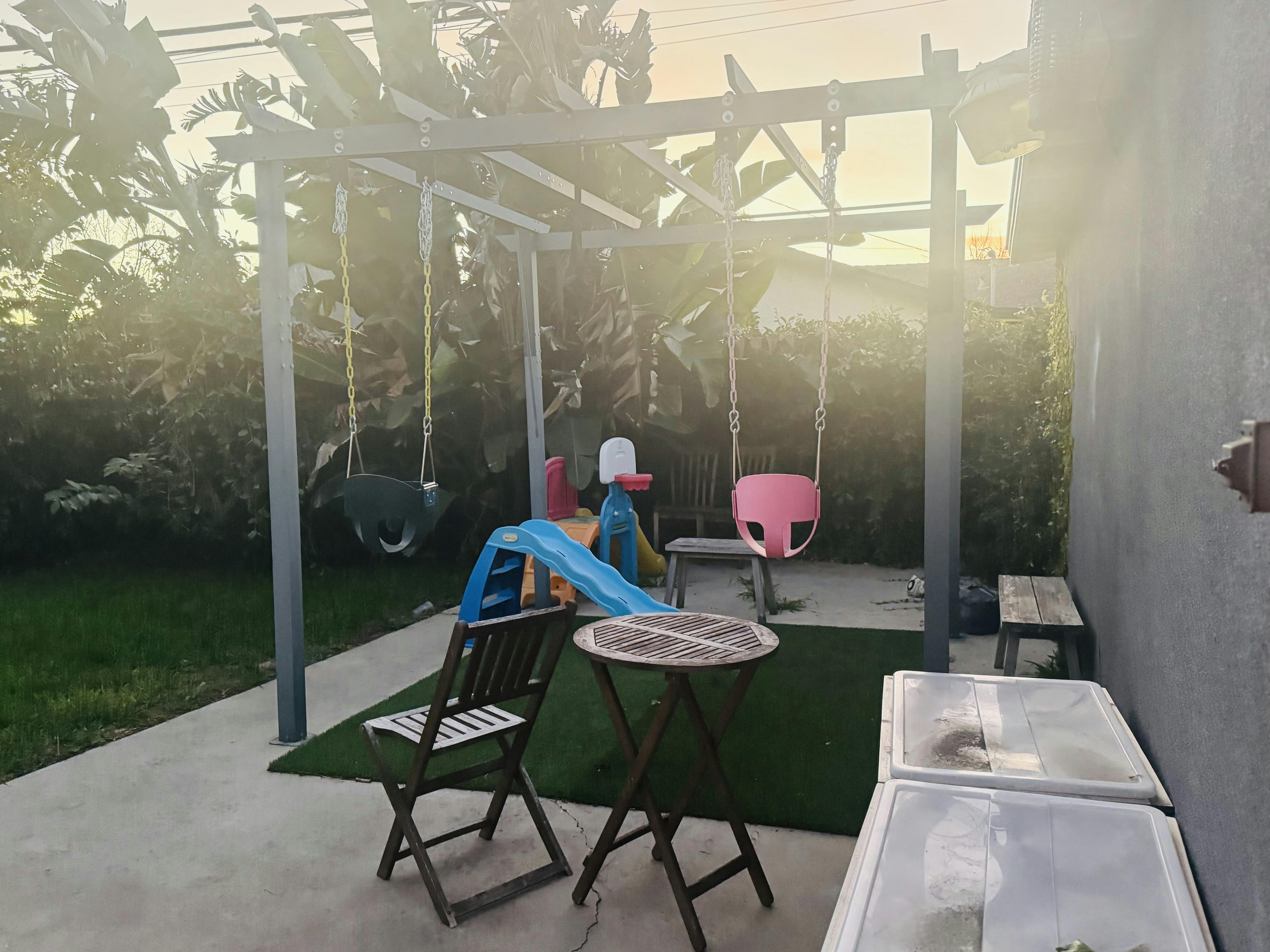 backyard patio with a swing set, blue slide, wooden table, and chairs