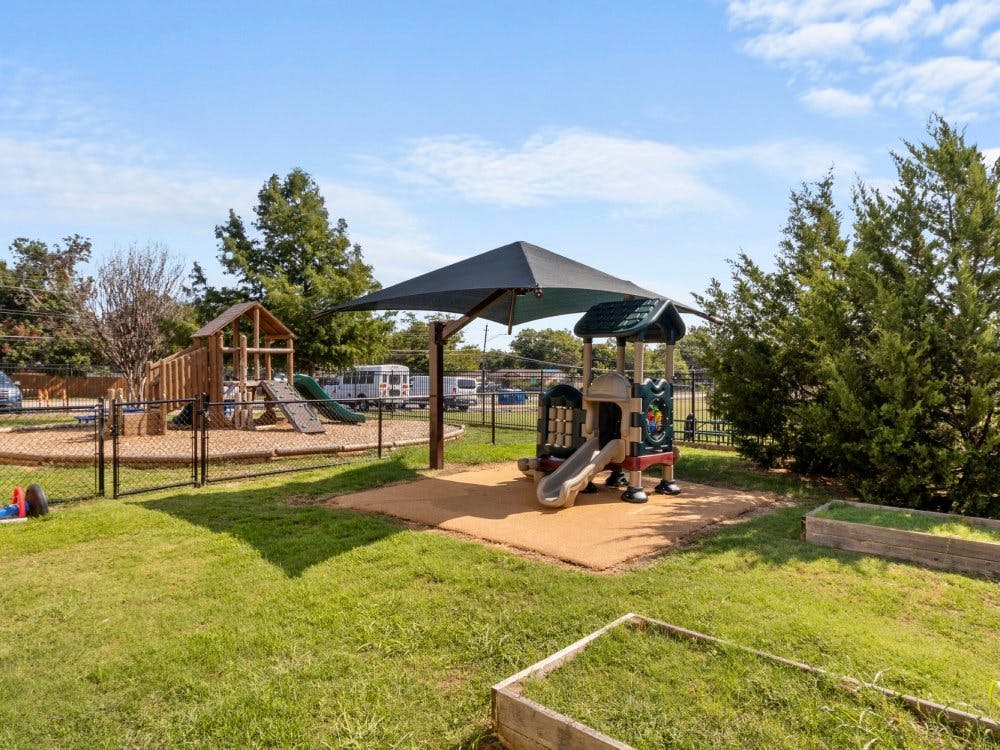 Playground area with various play structures, covered by a shade canopy