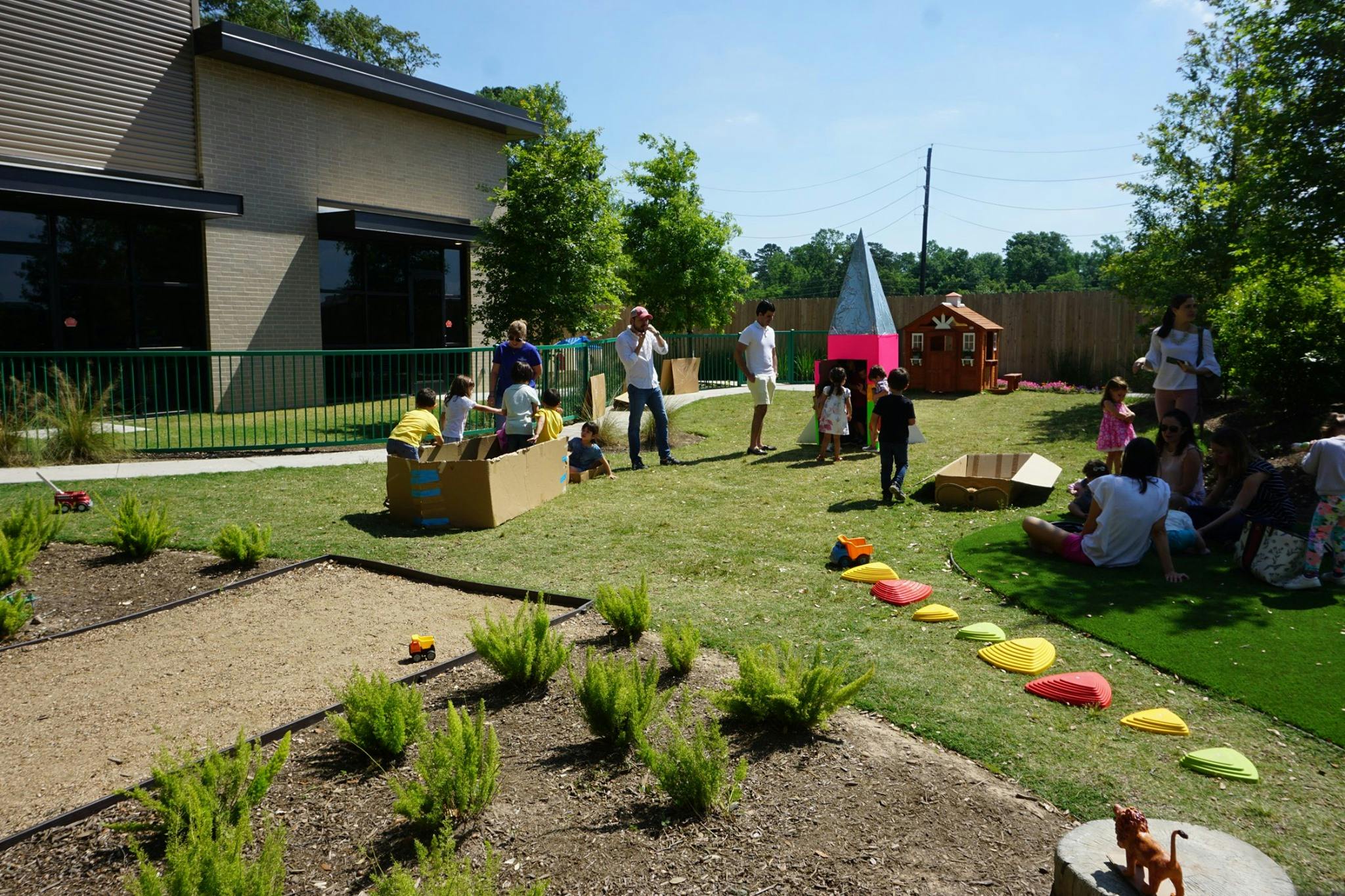 People and children gathered in a grassy outdoor area with a building