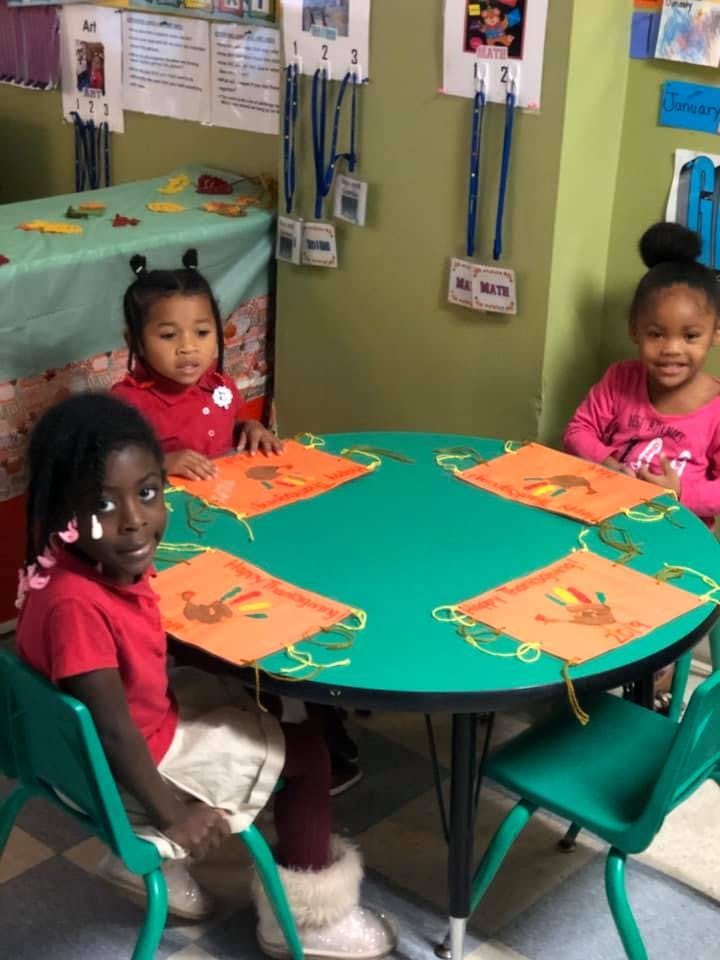 Three children sitting at a round table with craft projects