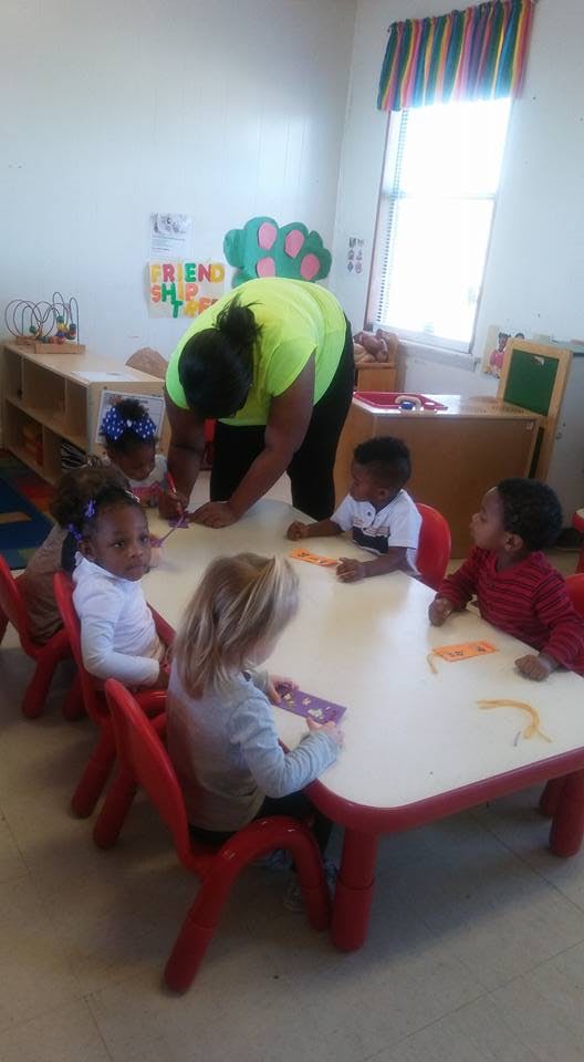 Adult helping children at a table in a classroom