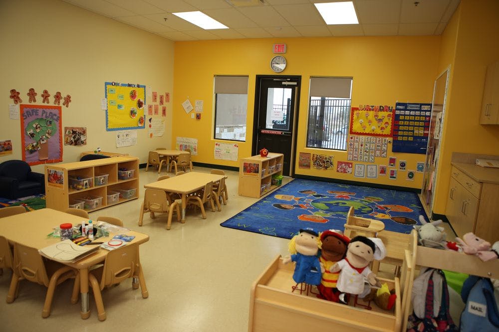 Classroom with small tables and chairs, a blue rug, and puppets