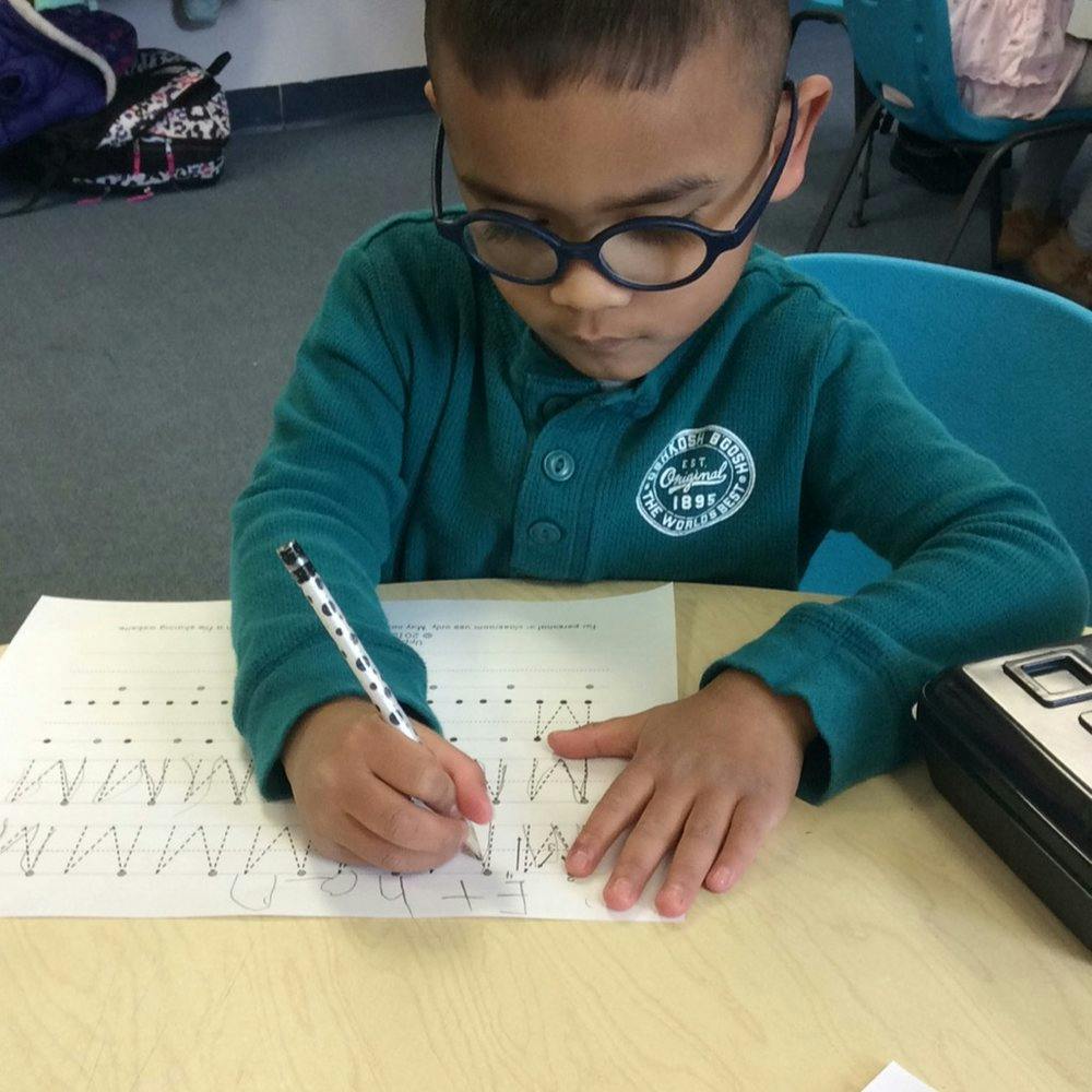 Child wearing glasses writing on a worksheet with a pencil at a desk