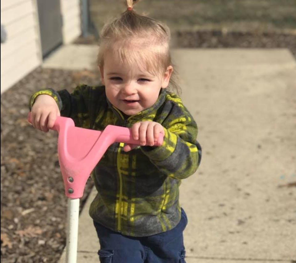 Child holding handlebars of a pink scooter