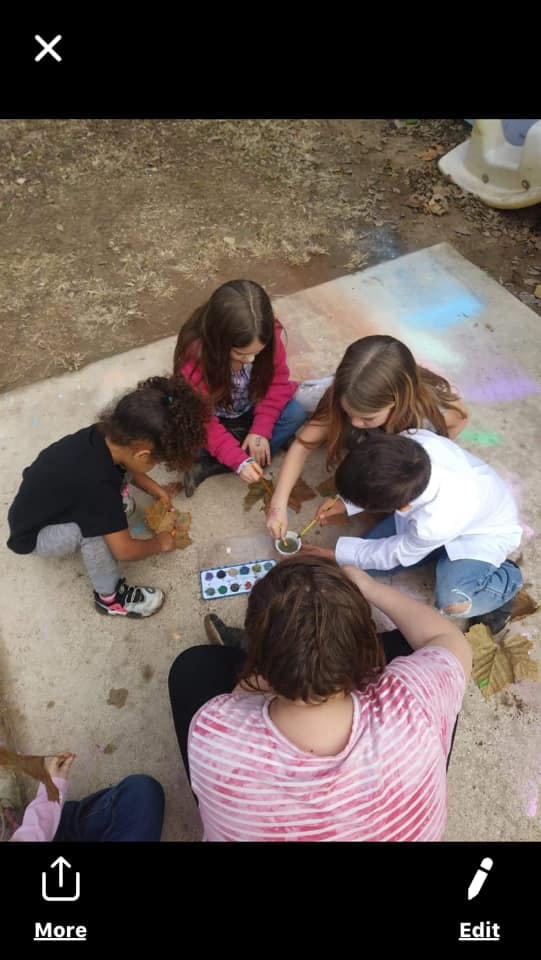 Children and an adult painting leaves on the ground