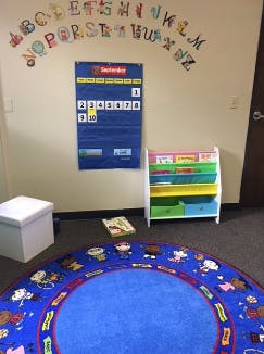 Classroom with alphabet on wall, calendar, bookshelf, and round rug