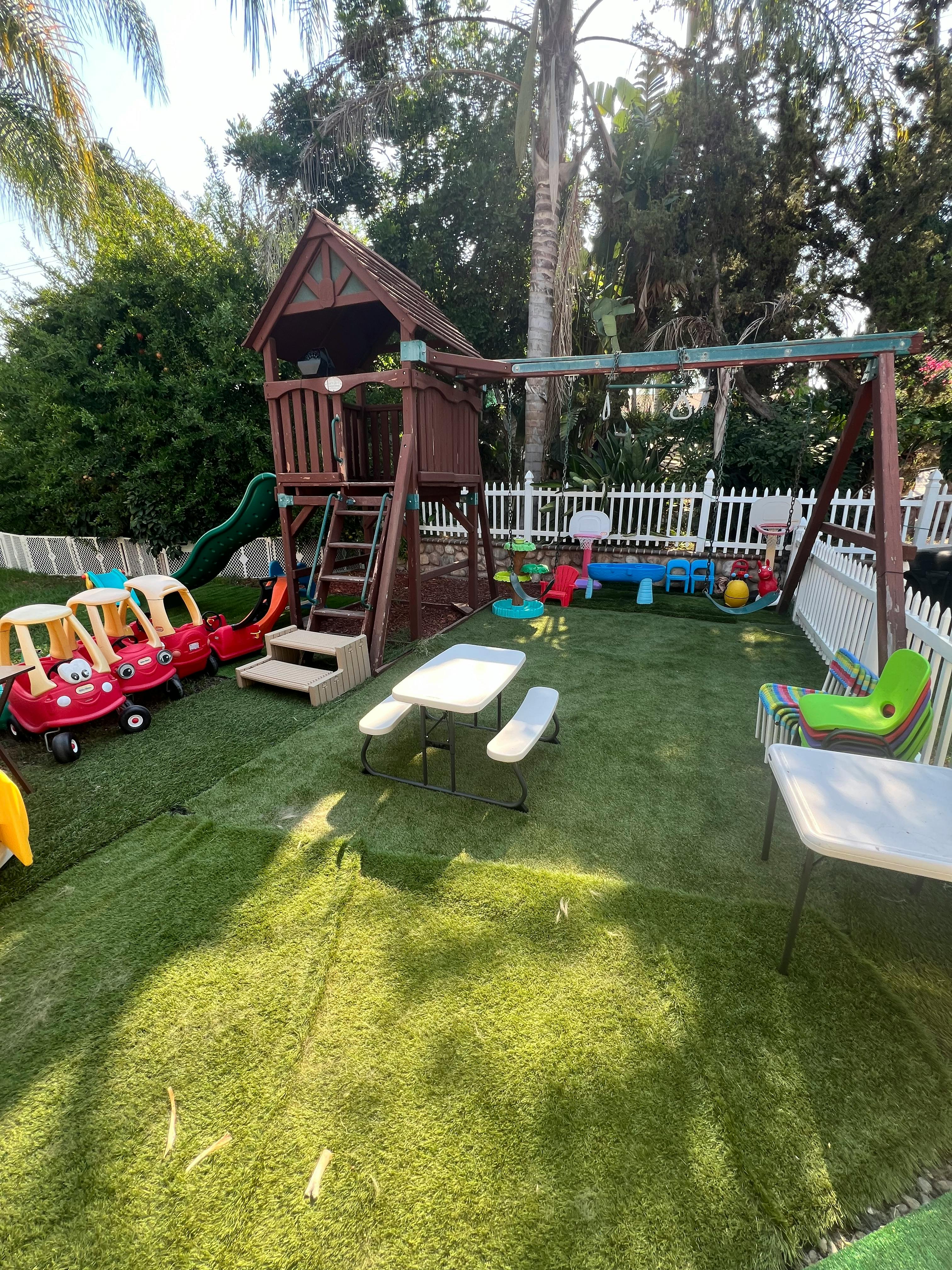 Outdoor play area with a wooden playset, swings, and ride-on toys