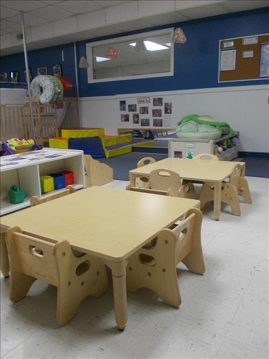 Classroom with small wooden tables and chairs, play mats, and a crib
