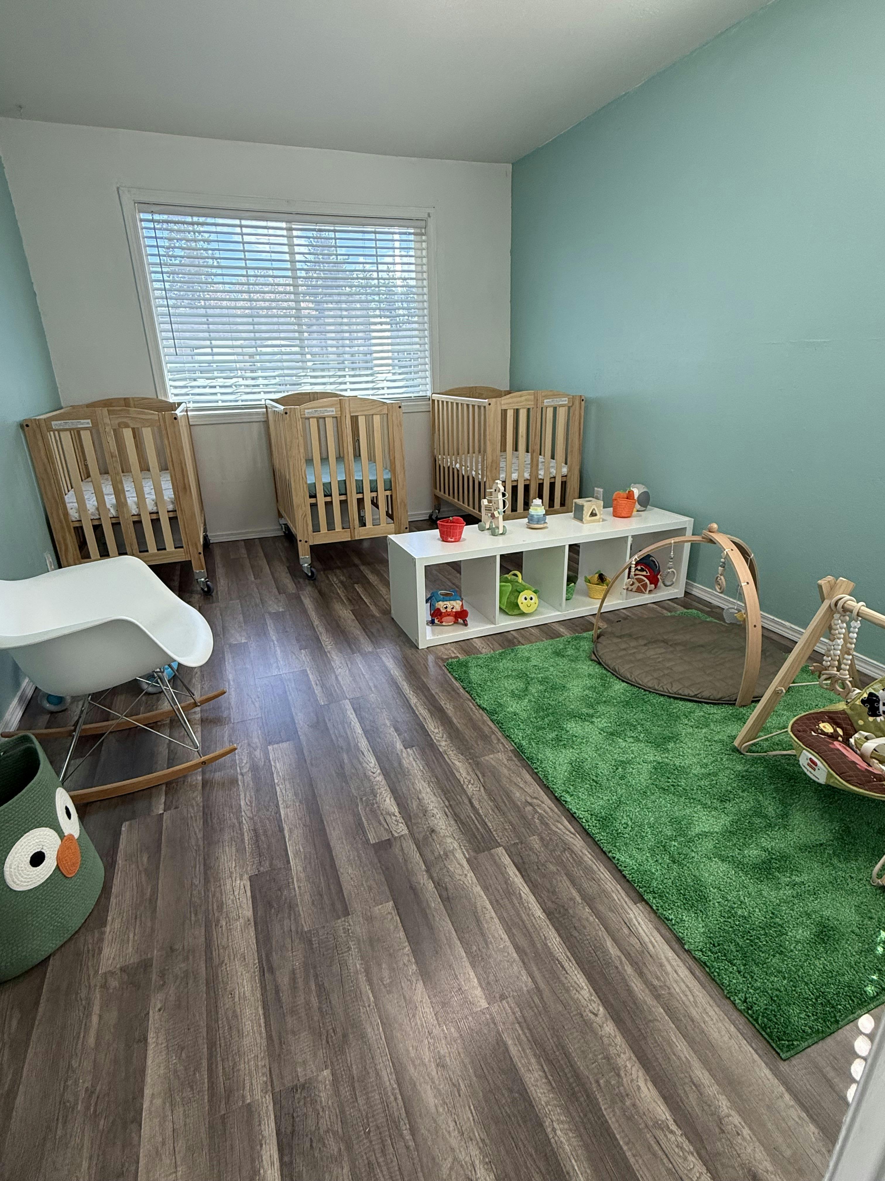 A nursery room with three wooden cribs, a rocking chair, and a play mat