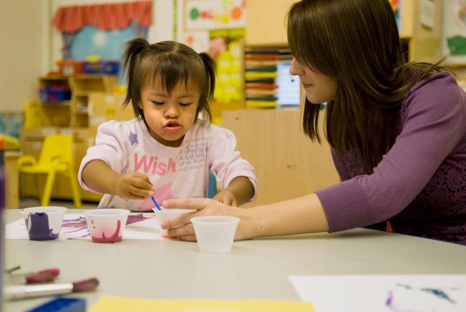 Child and person painting at a table in a classroom