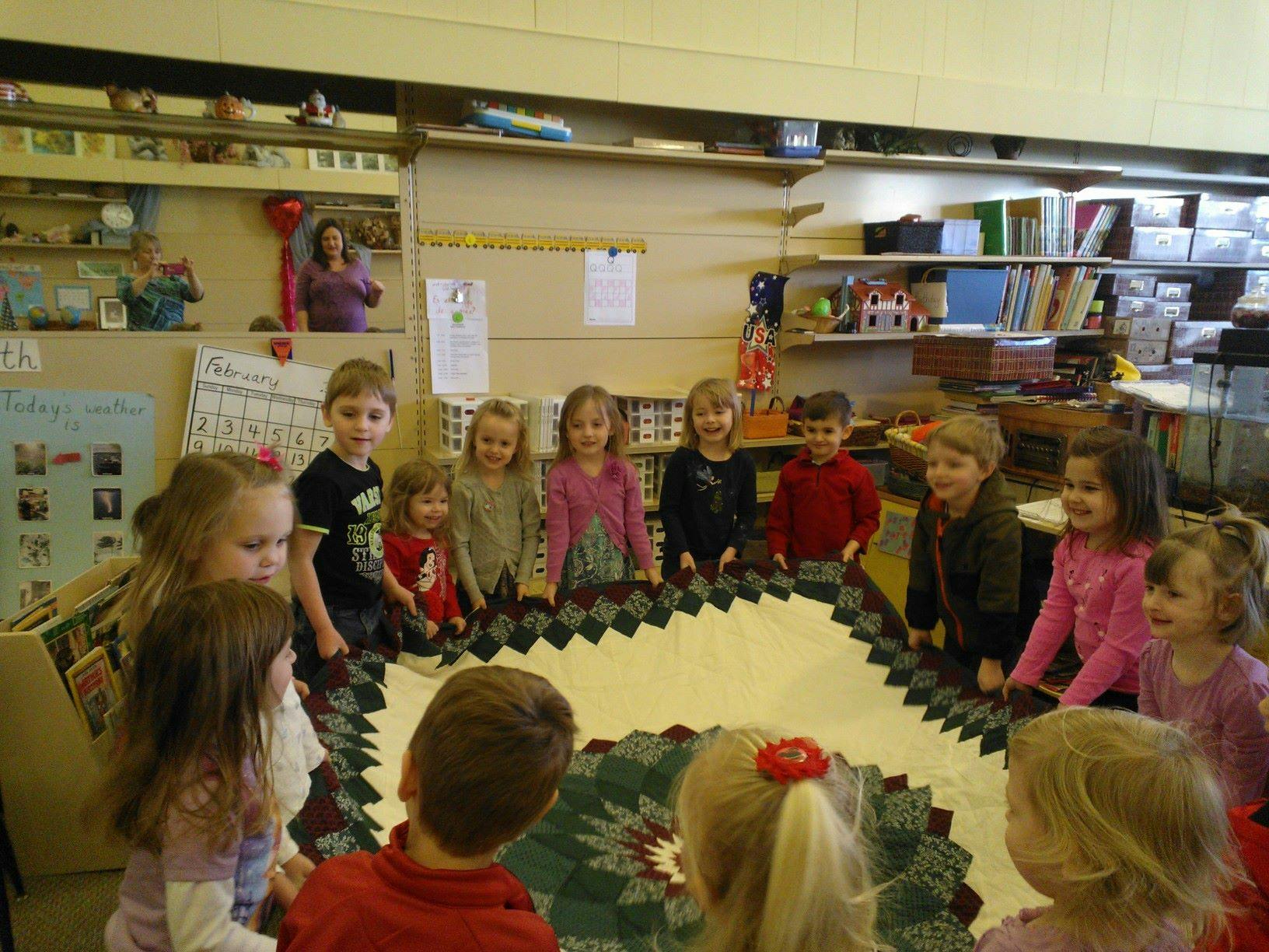 Children standing around a quilt in a classroom
