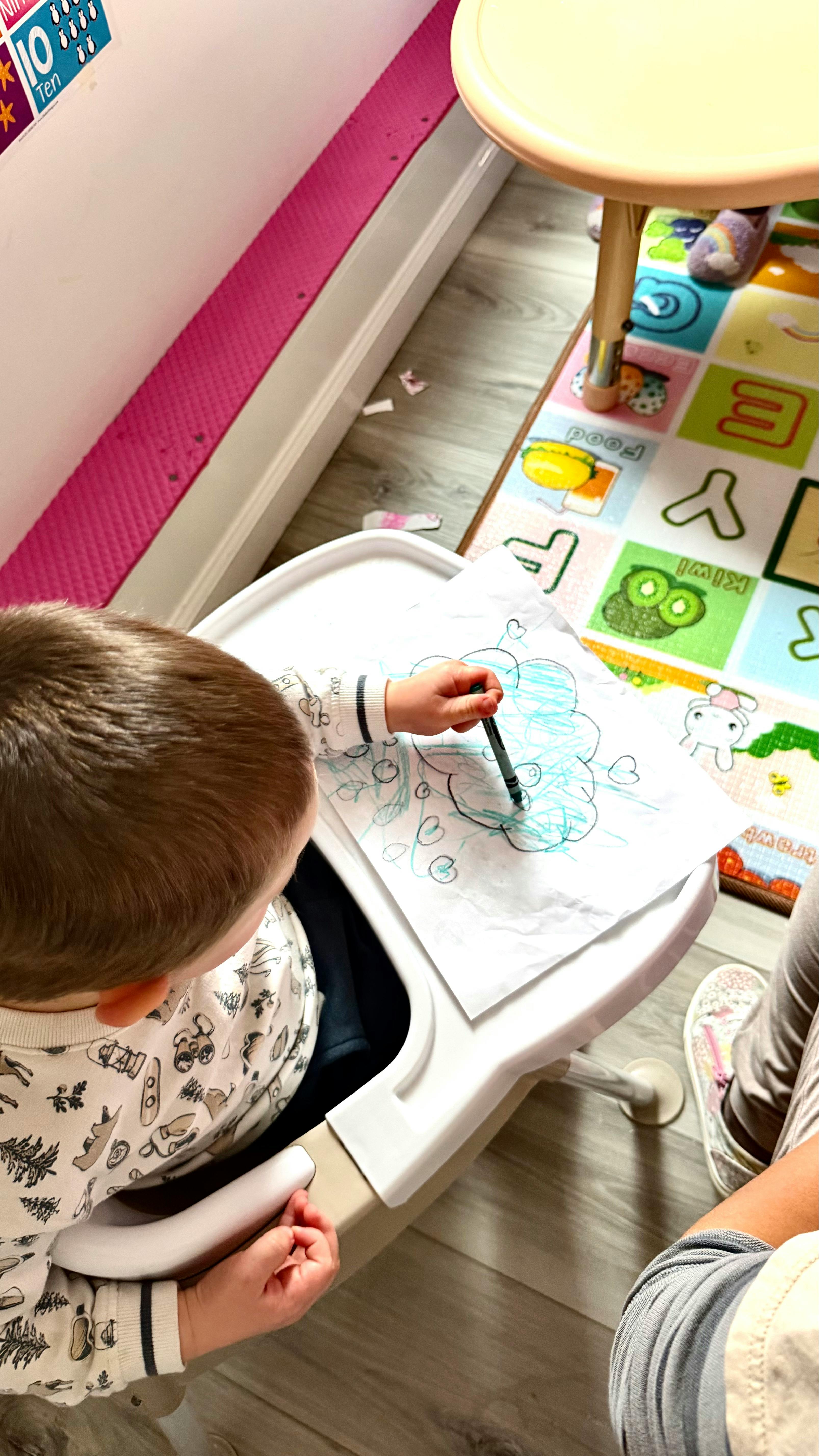Child drawing on paper with a crayon in a high chair