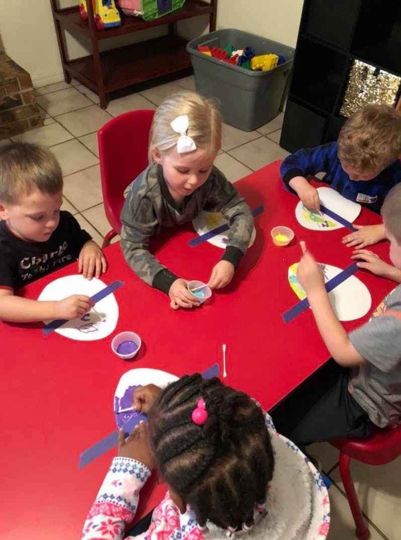 Children sitting at a red table doing crafts