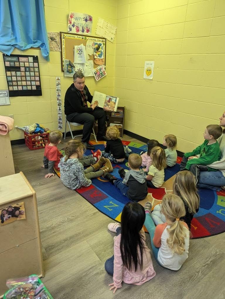 Person reading a book to a group of children sitting on a rug