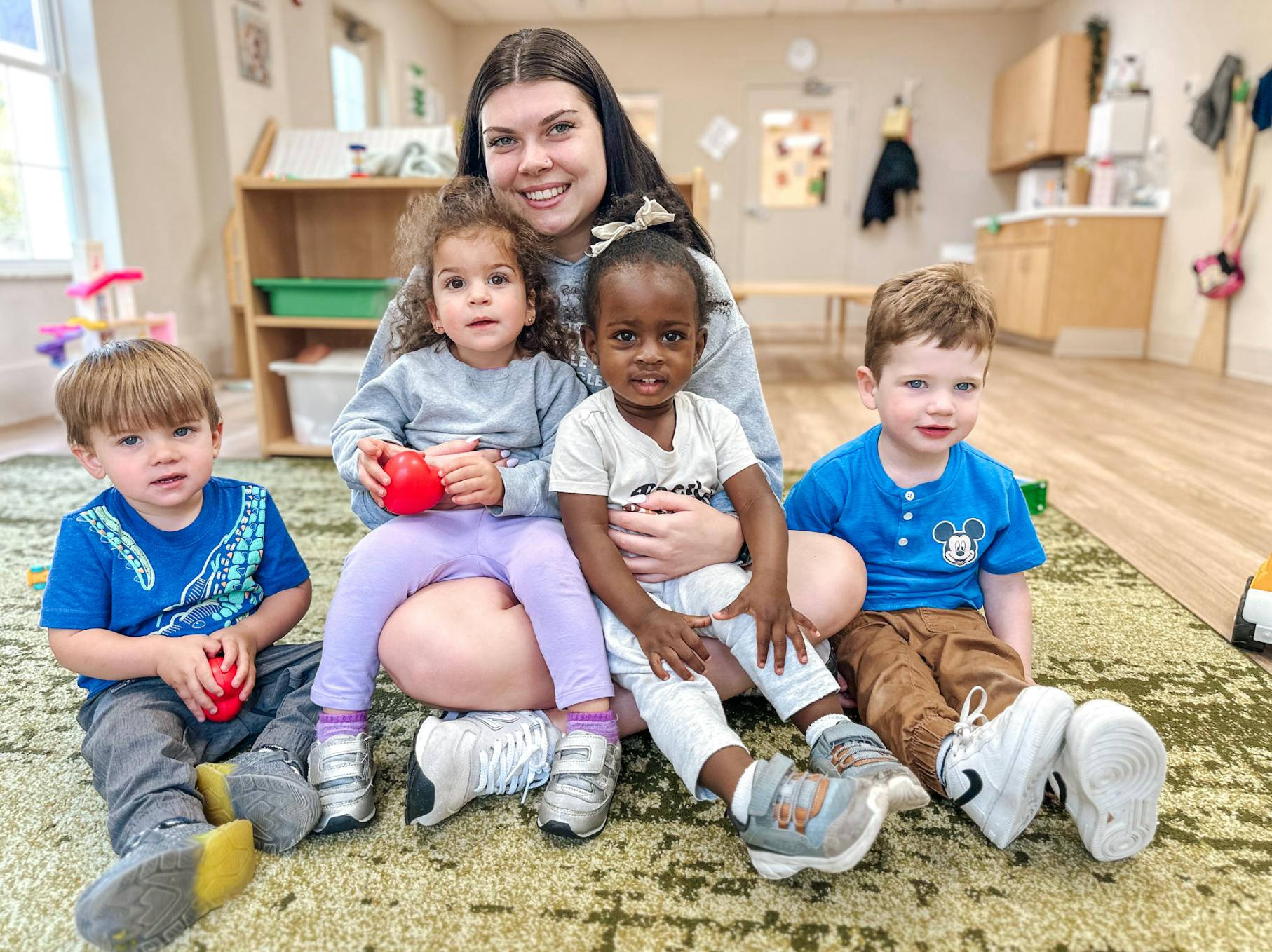 Person sitting on floor with four children in a classroom