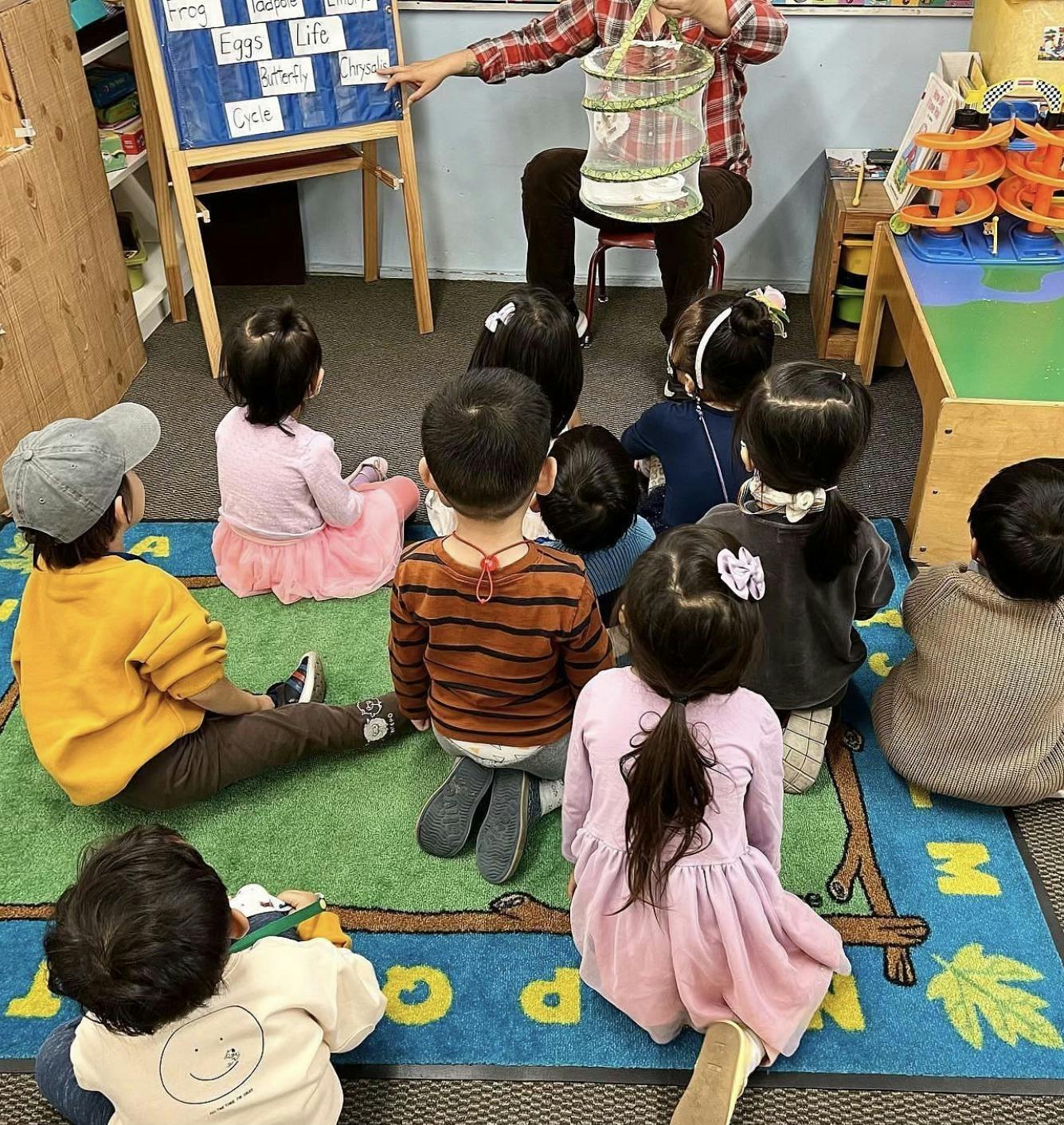 Adult holding a cage in front of children sitting on a rug