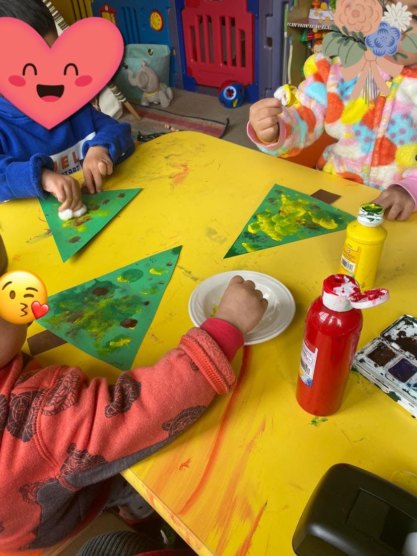 Children painting green paper triangles at a yellow table