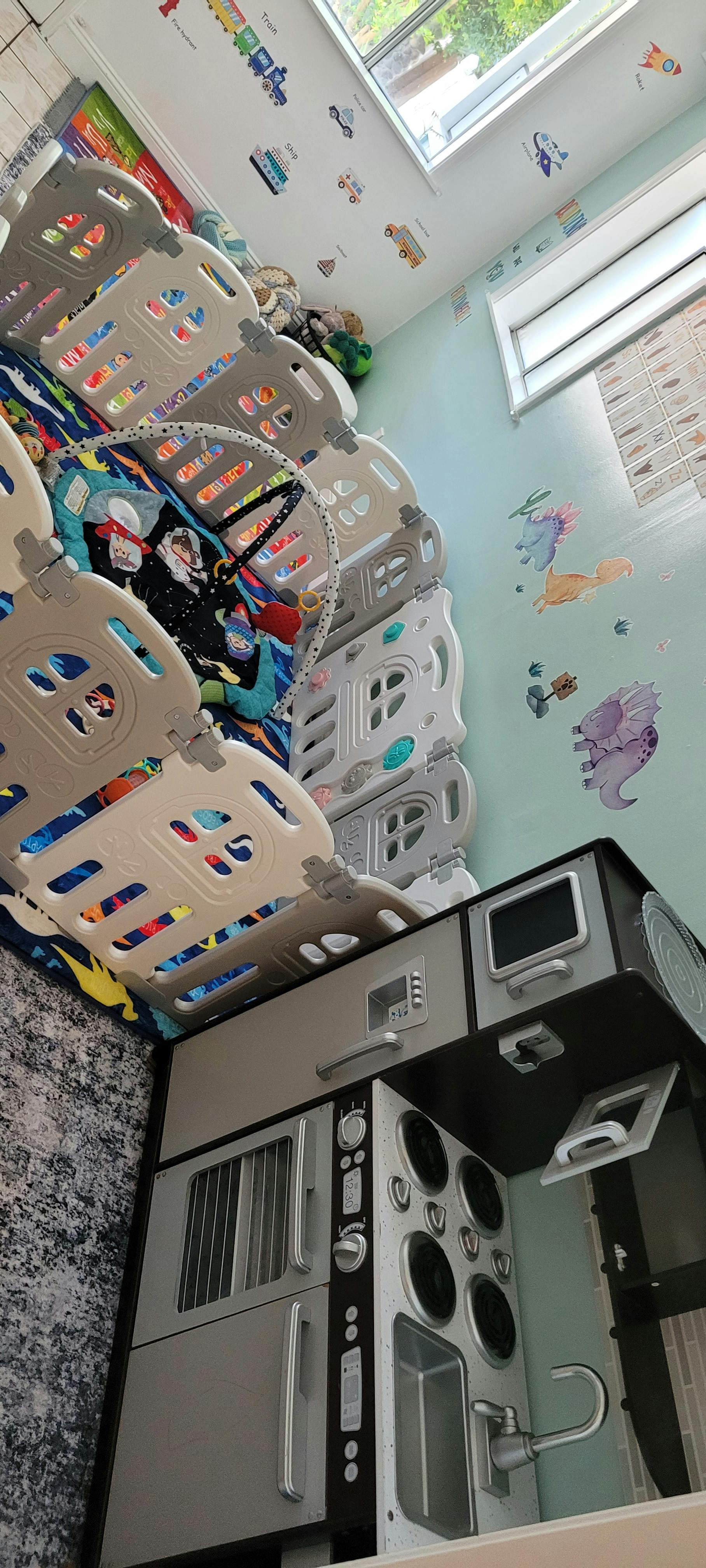 Playpen next to a toy kitchen set in a room with wall decals