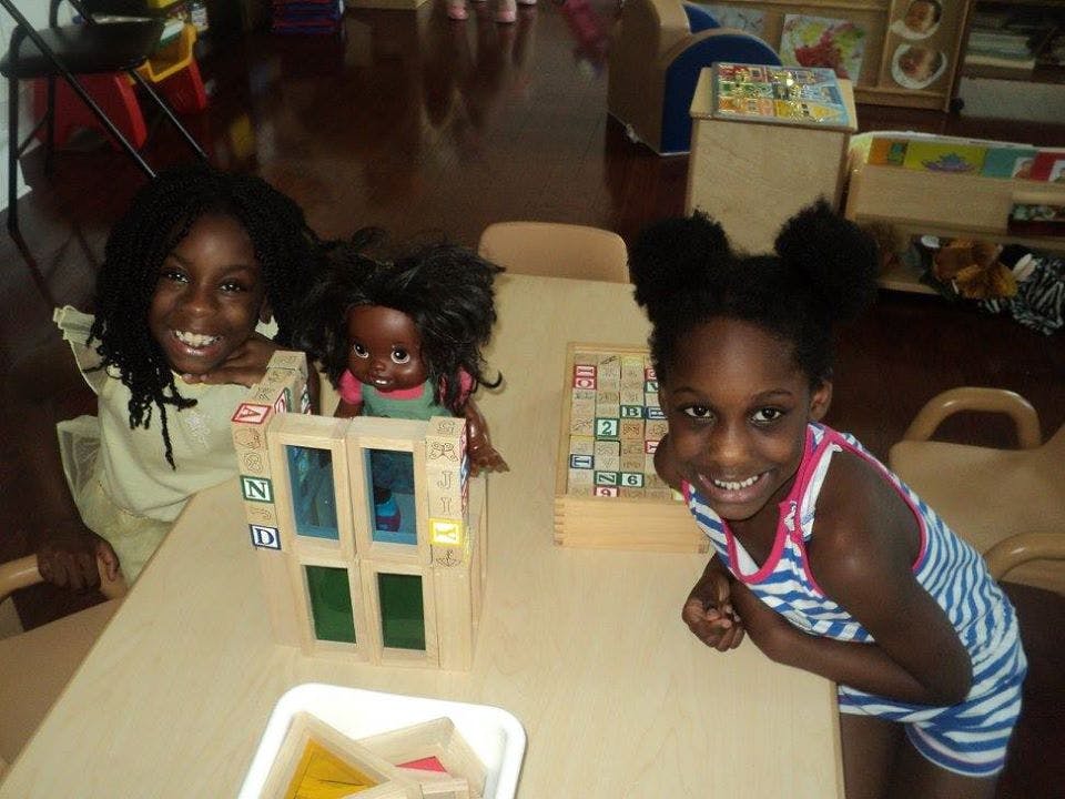 Two children playing with a doll and blocks at a table