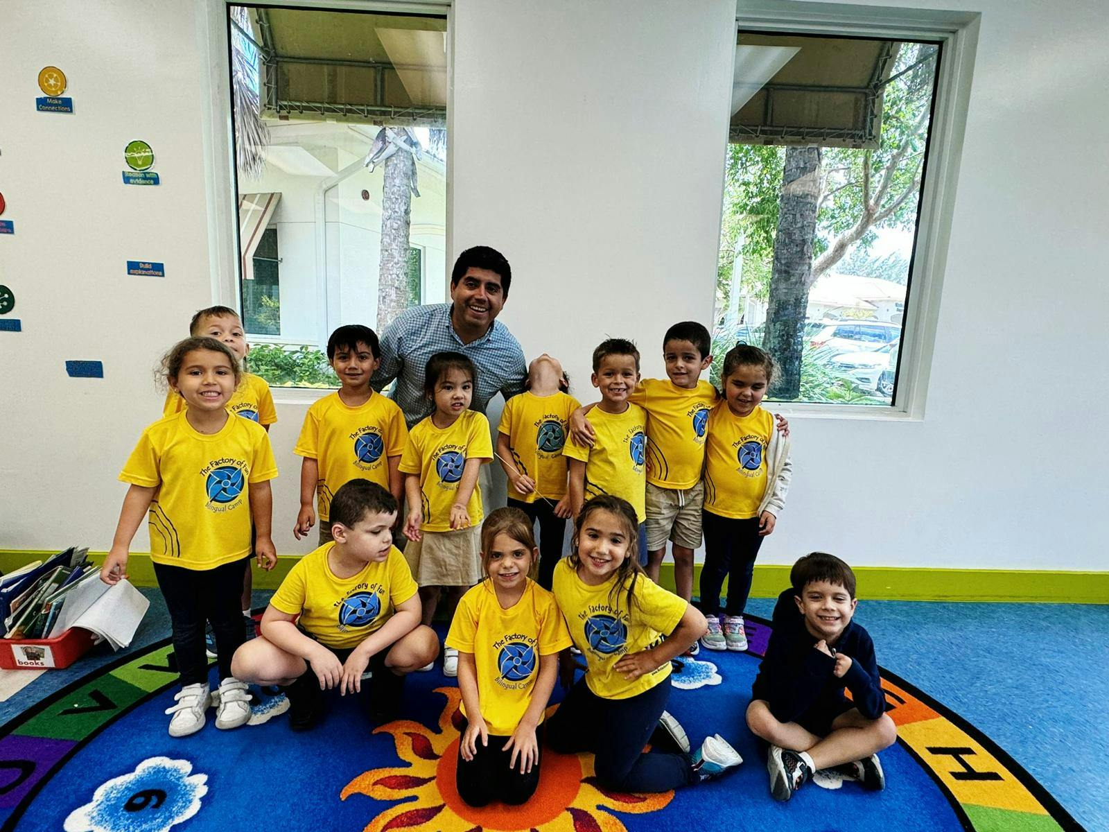 Adult and multiple children in yellow shirts posing in a classroom