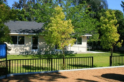 Building with a black roof and light-colored walls behind a black fence