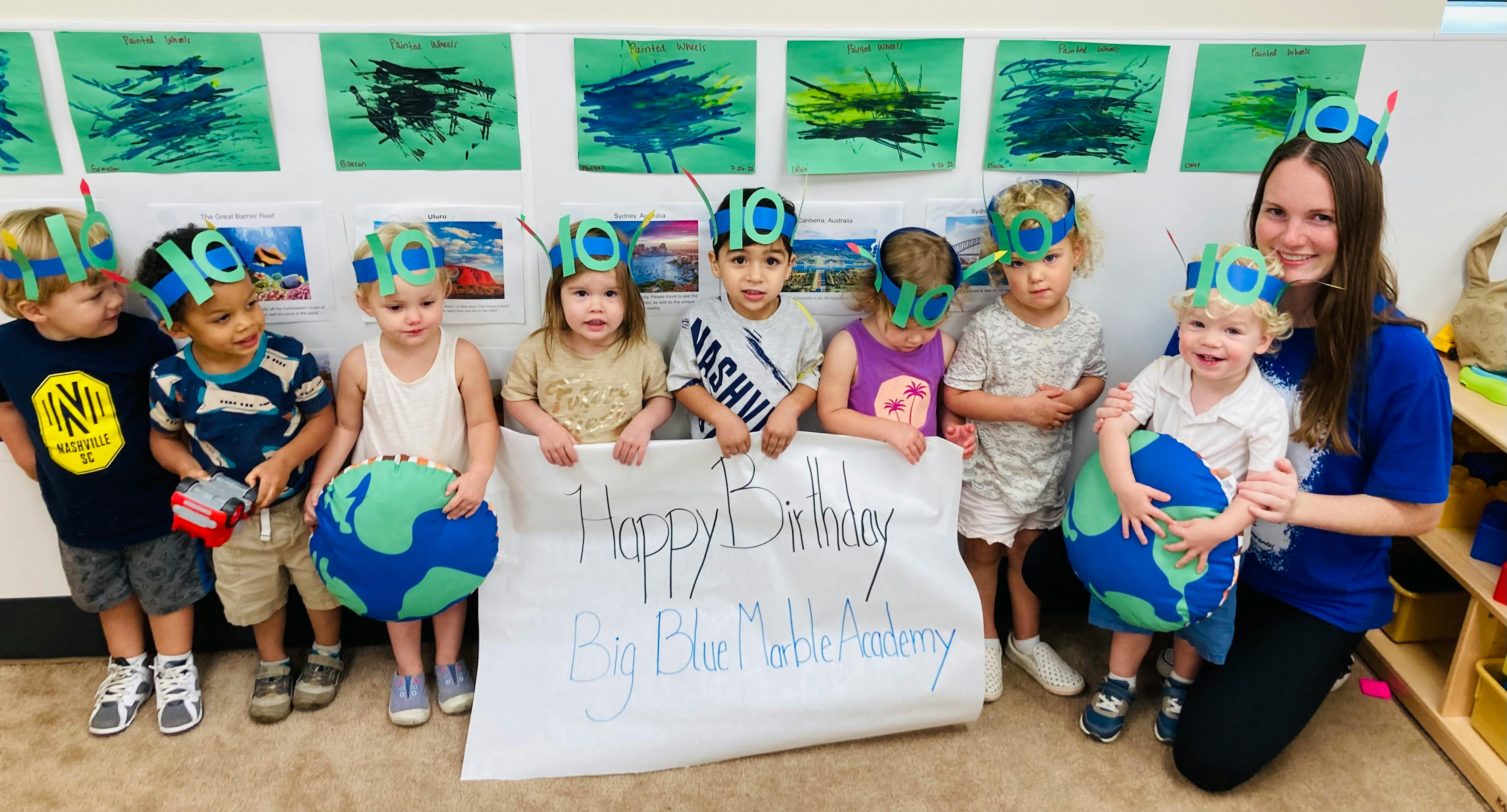 Adult and children wearing paper crowns, holding a sign and globe