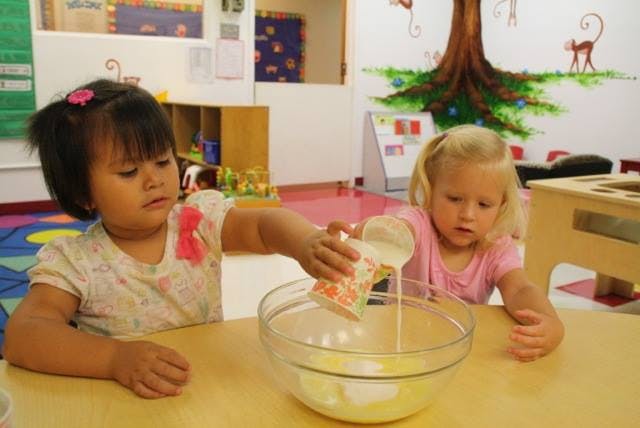 Two children pouring liquid from a cup into a bowl