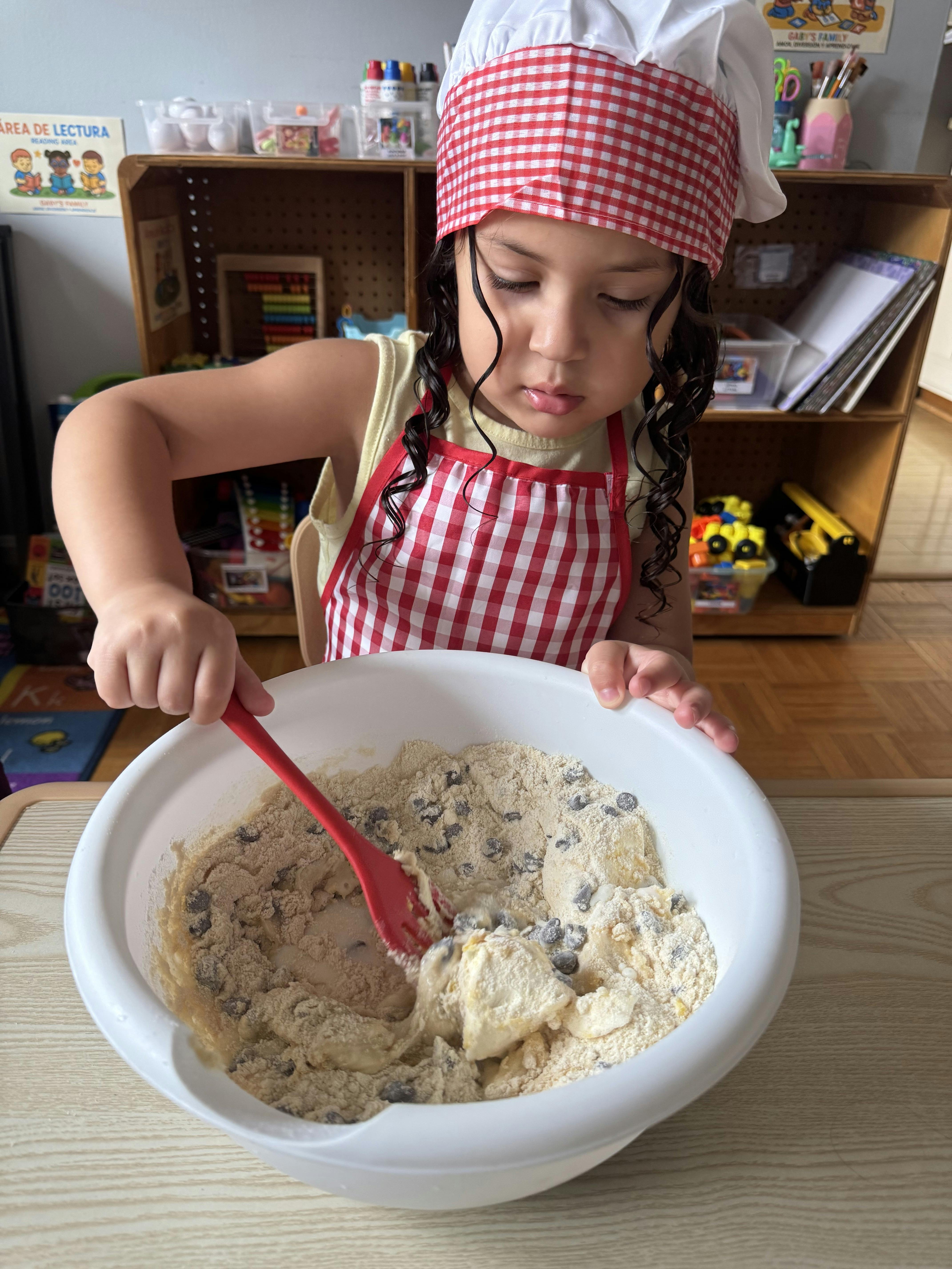 Child in chef hat and apron mixing ingredients in a bowl