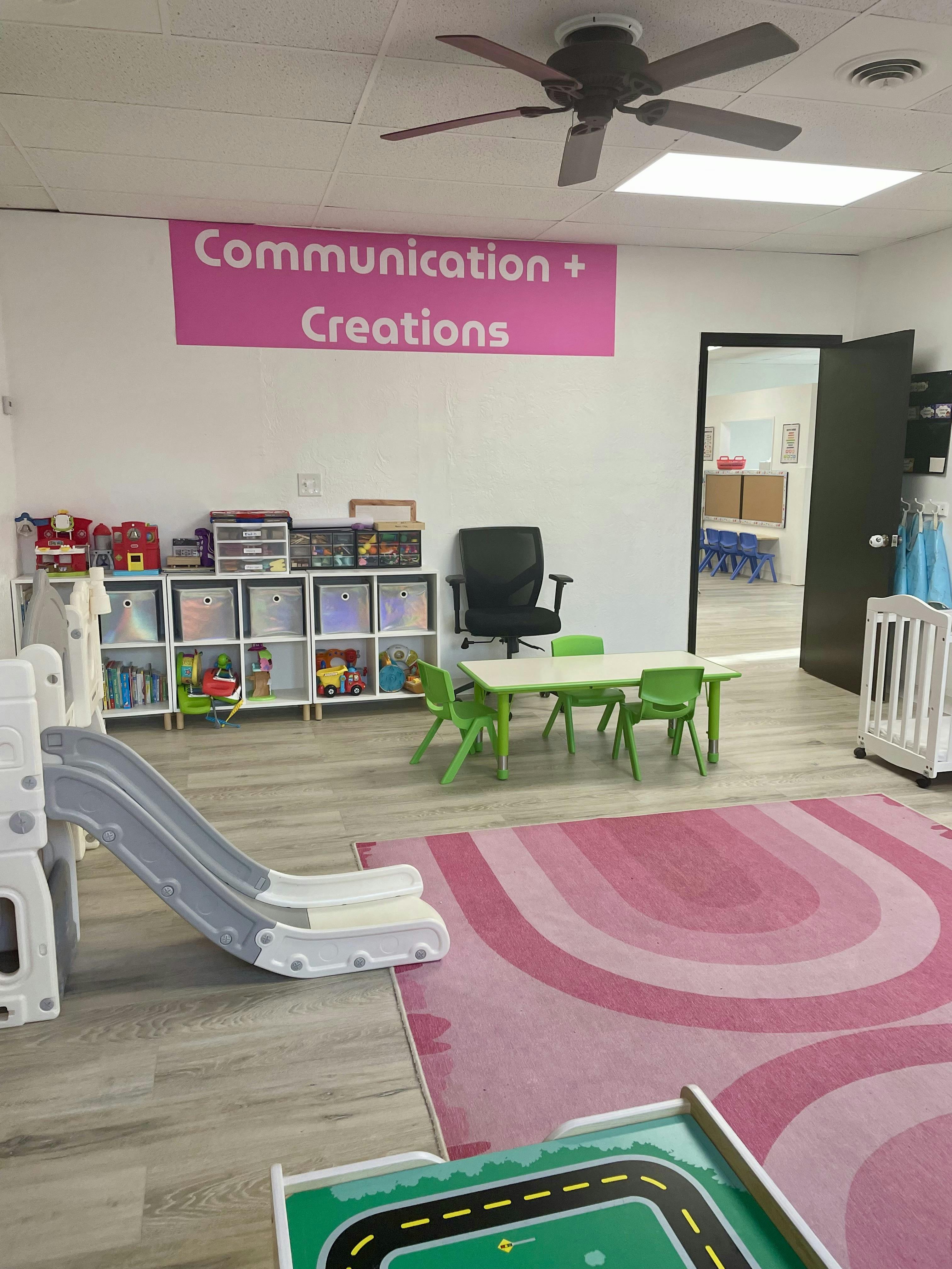 Playroom with a pink rug, a small slide, and a Communication + Creations sign