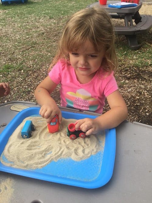 Child playing with toy trains in a sand tray
