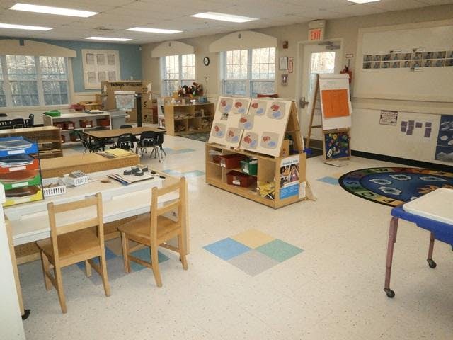 Classroom with child-sized tables and chairs, shelves with toys, and an easel