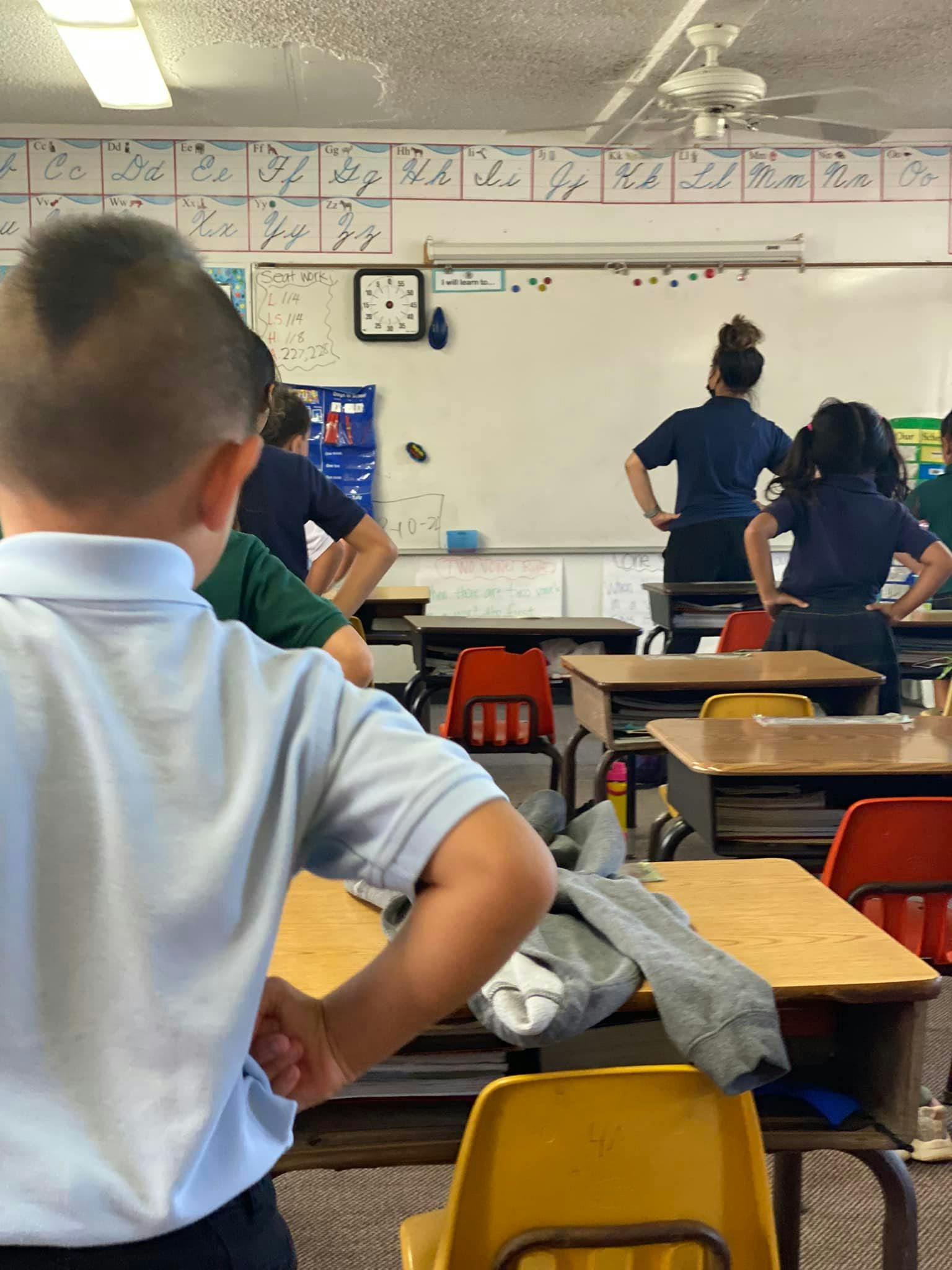 Children and adults standing in a classroom with hands on hips
