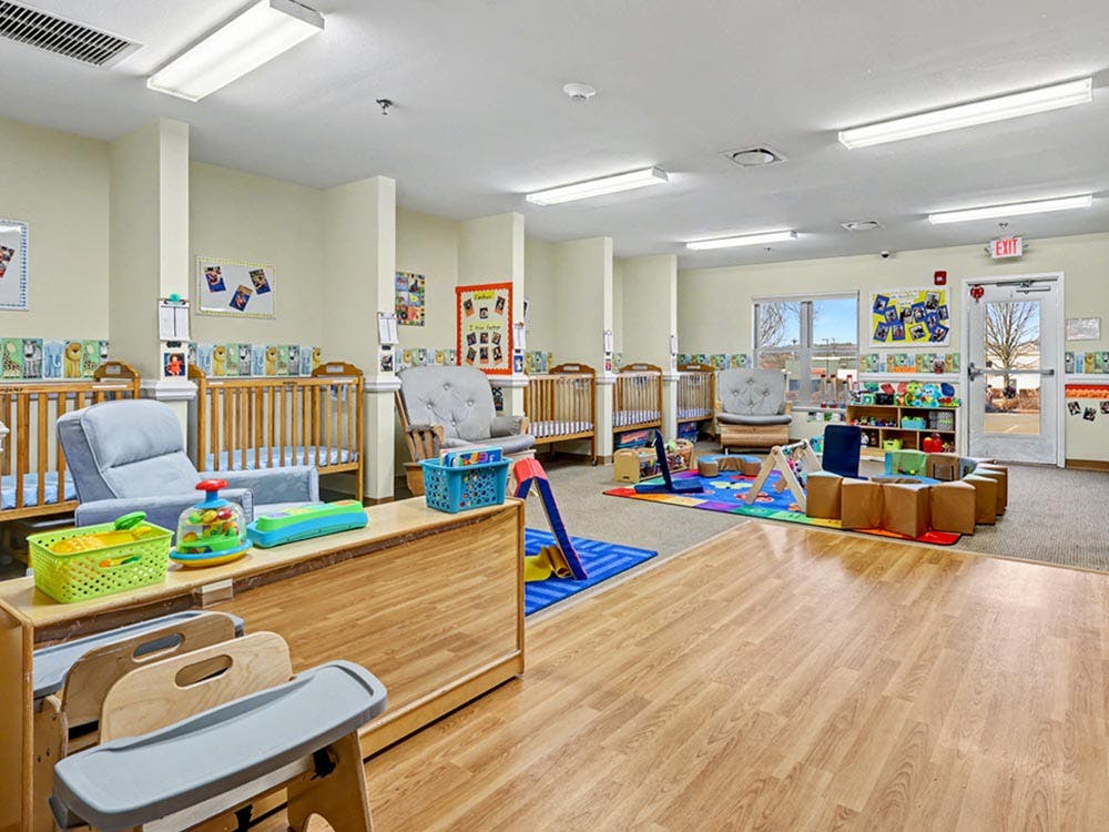 A brightly lit nursery room with several cribs, rocking chairs, and play areas
