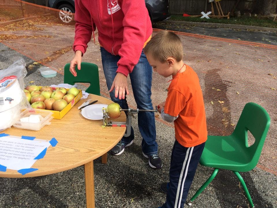 Person and child using an apple peeler at a table with apples