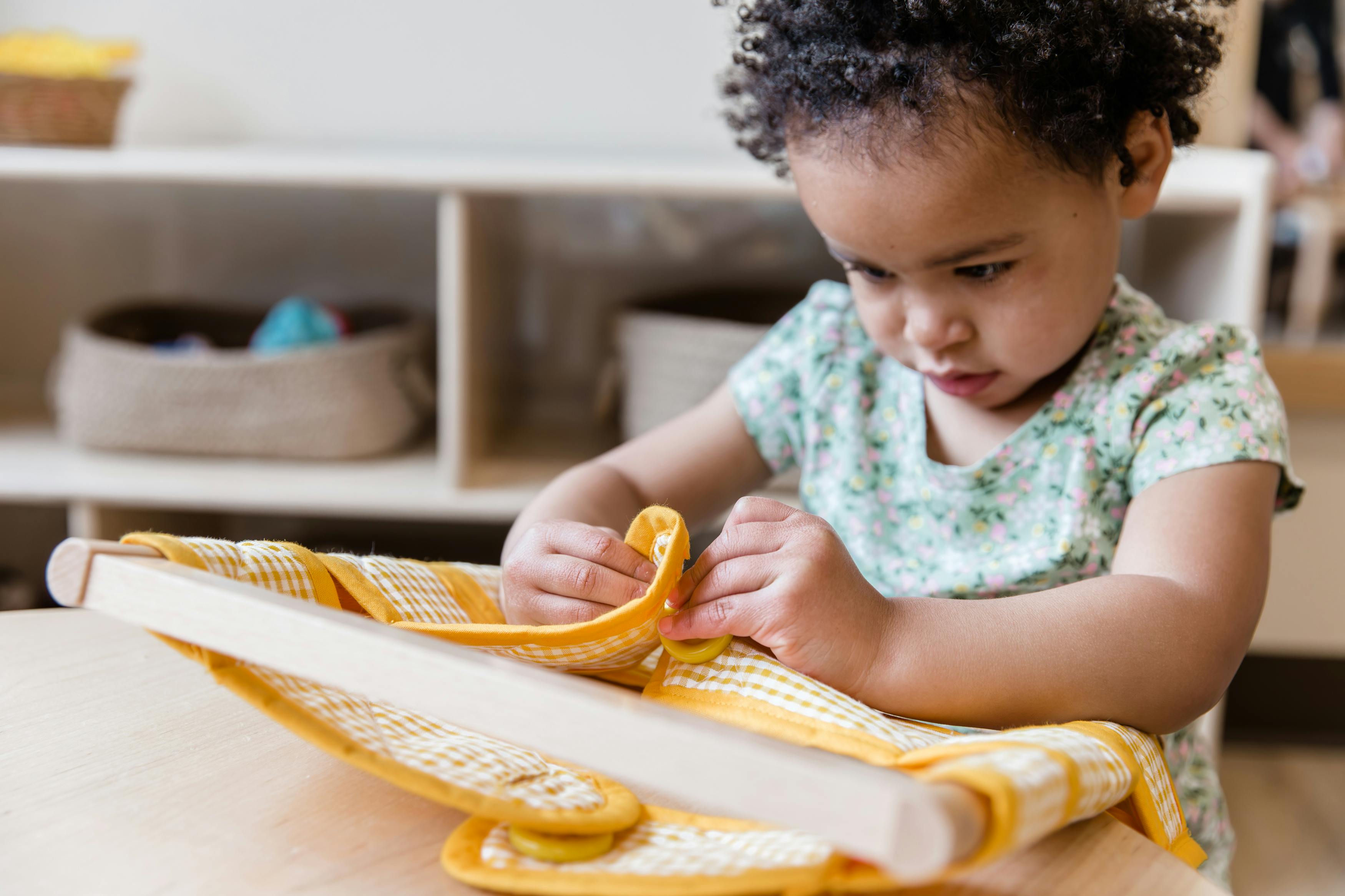 Child folding a yellow cloth on a wooden frame
