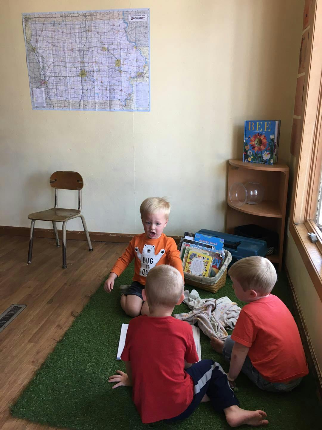 Three children sitting on a green rug in a room