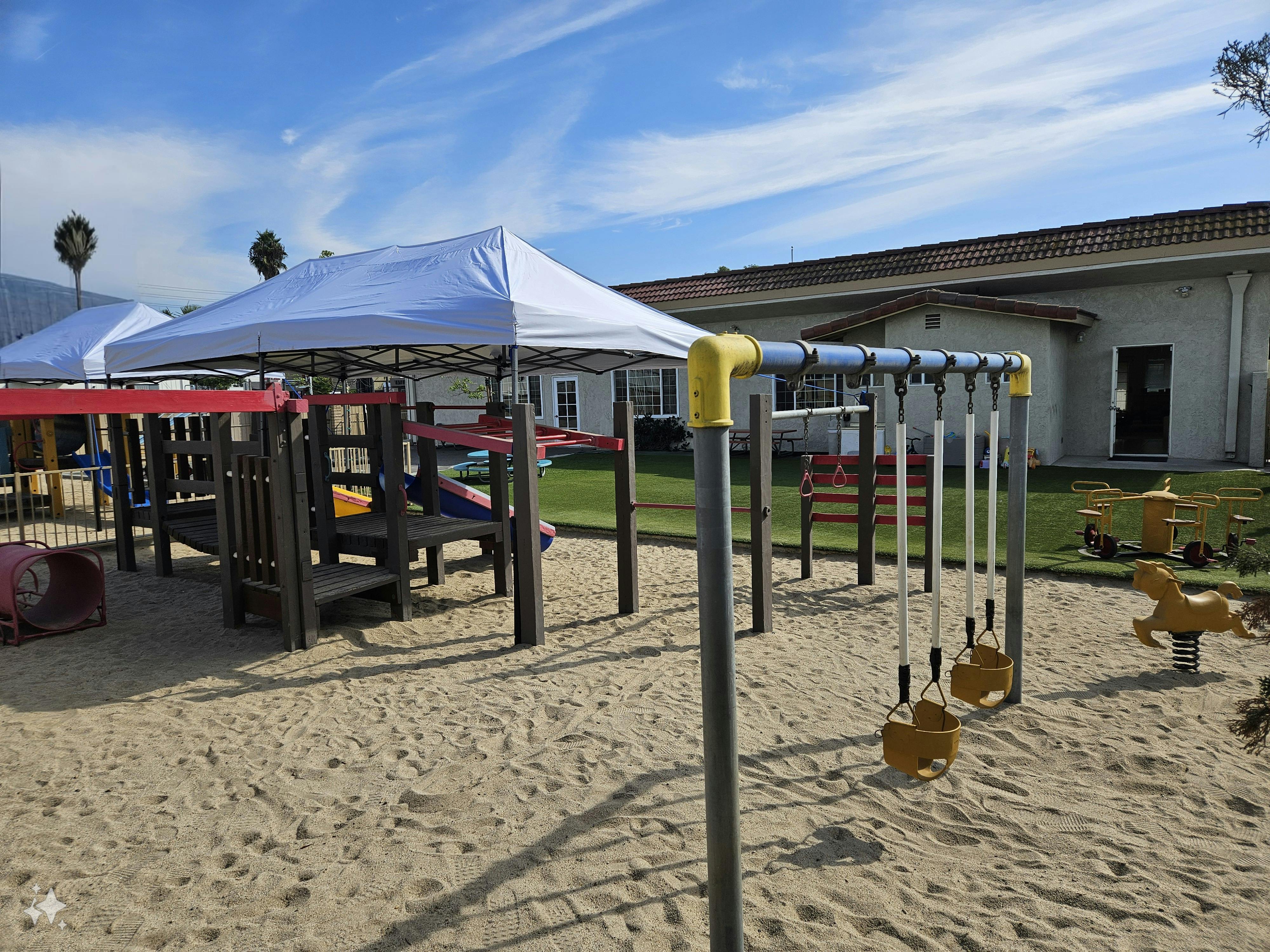 Playground with sand, swings, and play structure under a white canopy