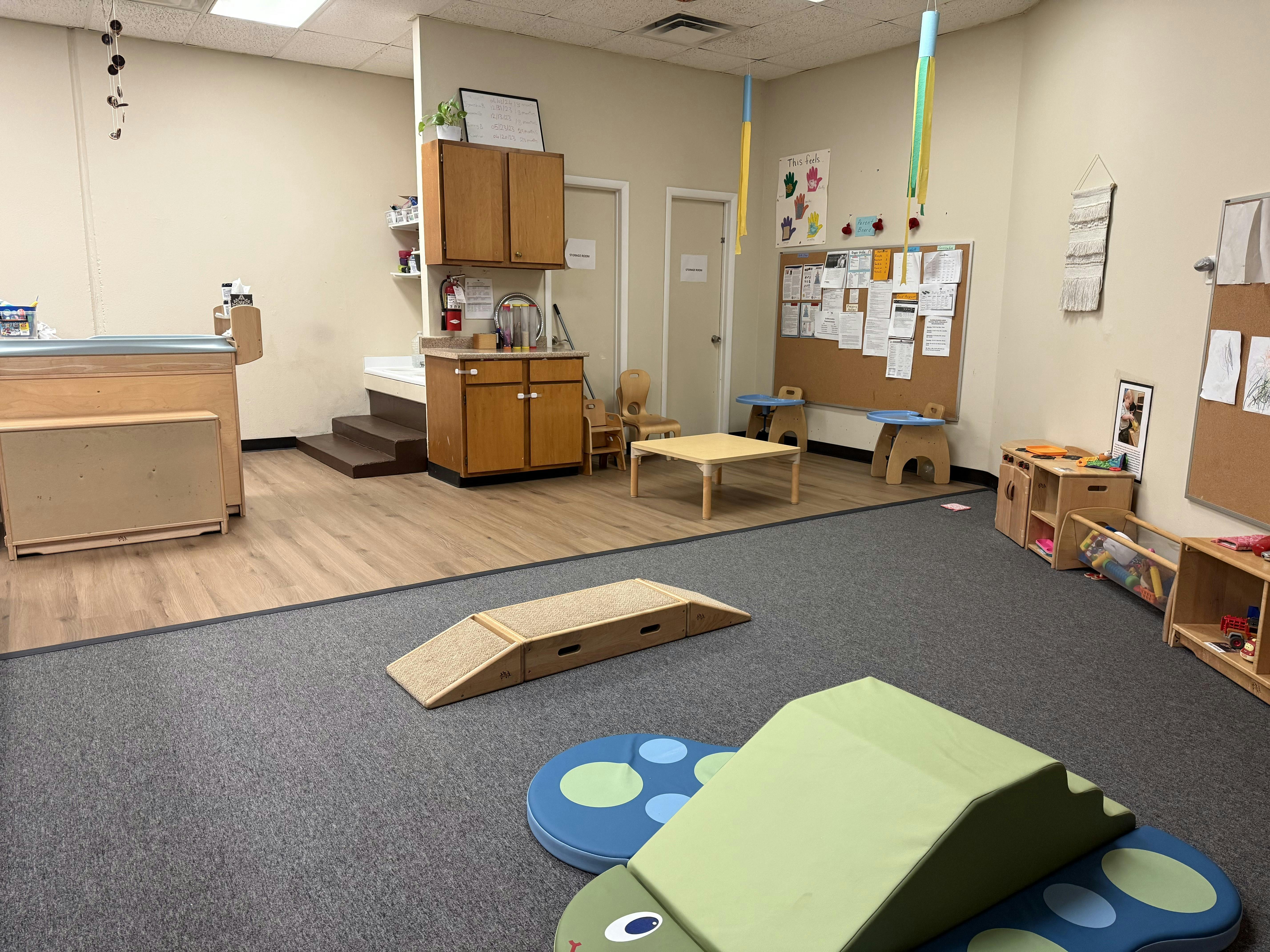 Indoor play area with carpet and wood flooring, small tables, and play equipment