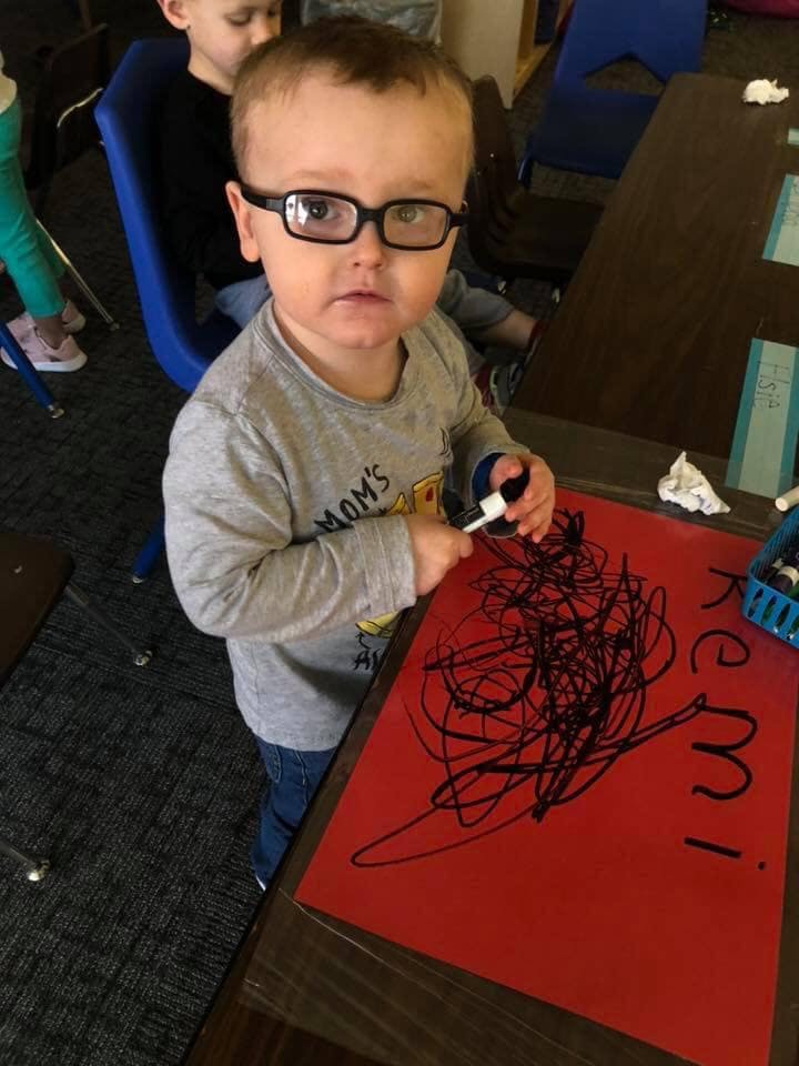Child in glasses drawing on red paper with a marker